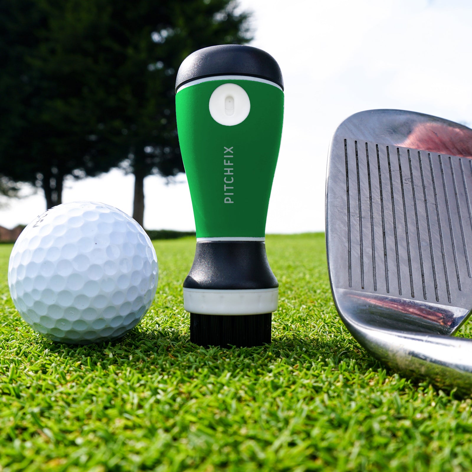 Green and black Aquabrush golf club cleaner with built-in water spray displayed on grass next to golf ball and iron club head