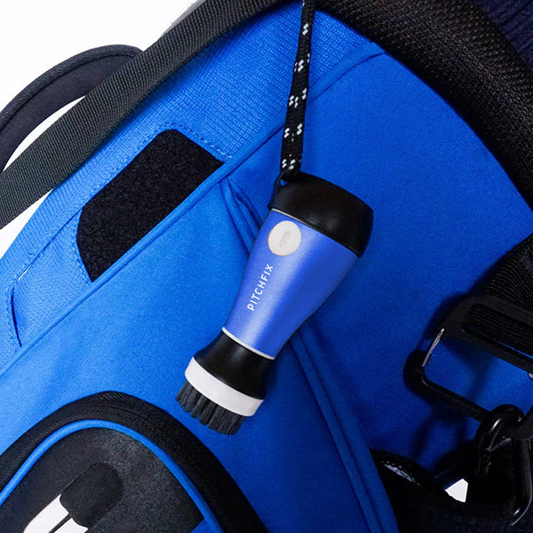 Blue golf club brush with integrated water spray system hanging from black lanyard attached to golf bag, featuring black rubber grip and white accents