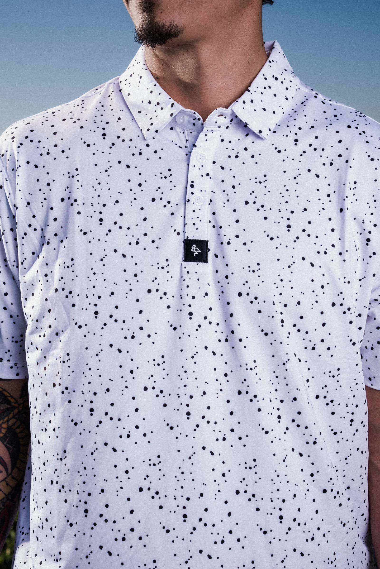 Men’s white polo with subtle grey-black dot “cosmic sprinkle” pattern—sleek, breathable, and performance-ready.
