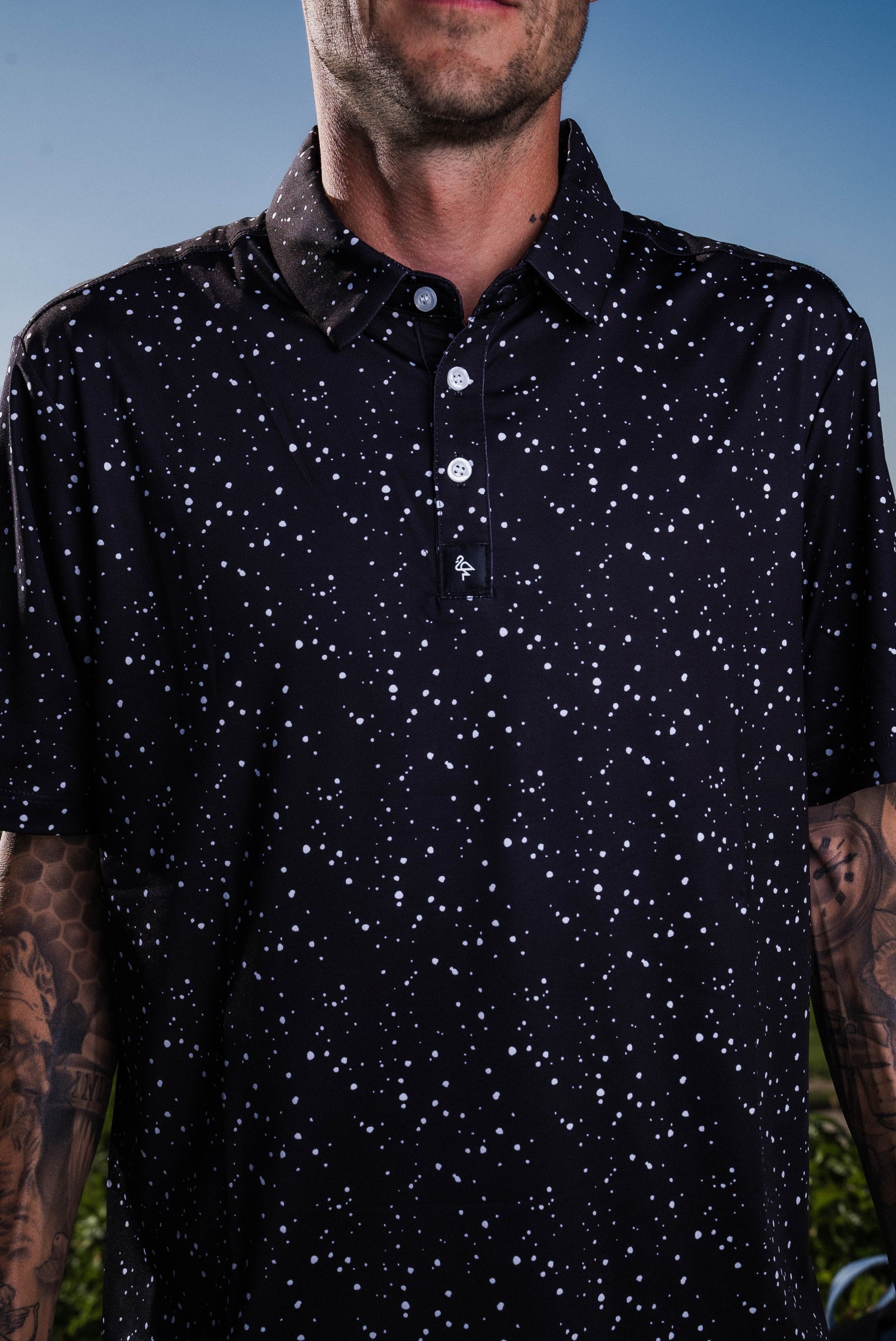 Men’s black polo with subtle gray-white speckle “cosmic sprinkle” print – sleek, breathable, stretch-performance ready.