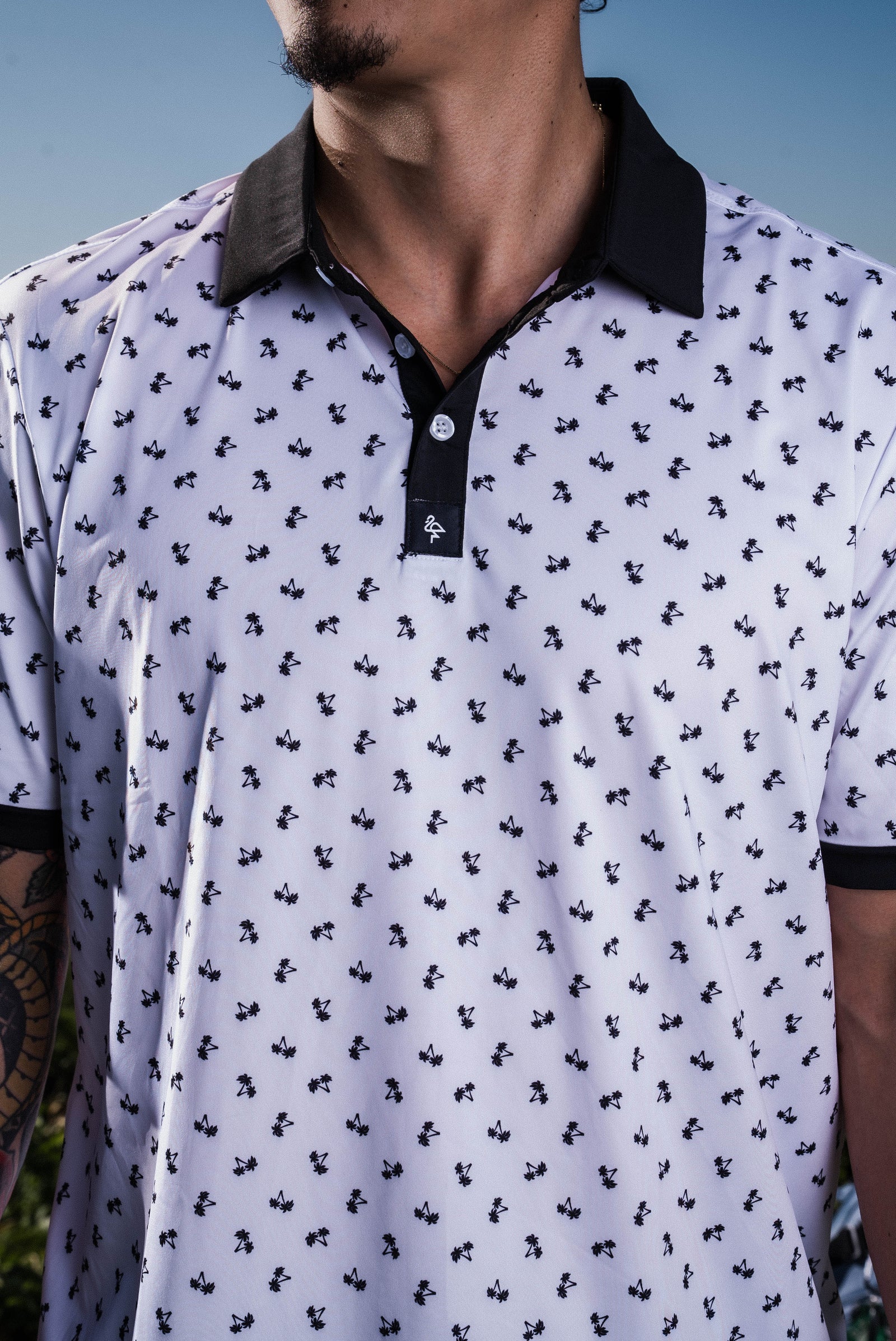 Men’s white polo with small navy palm leaf print and contrast collar – tropical-infused, stretch-performance ready.