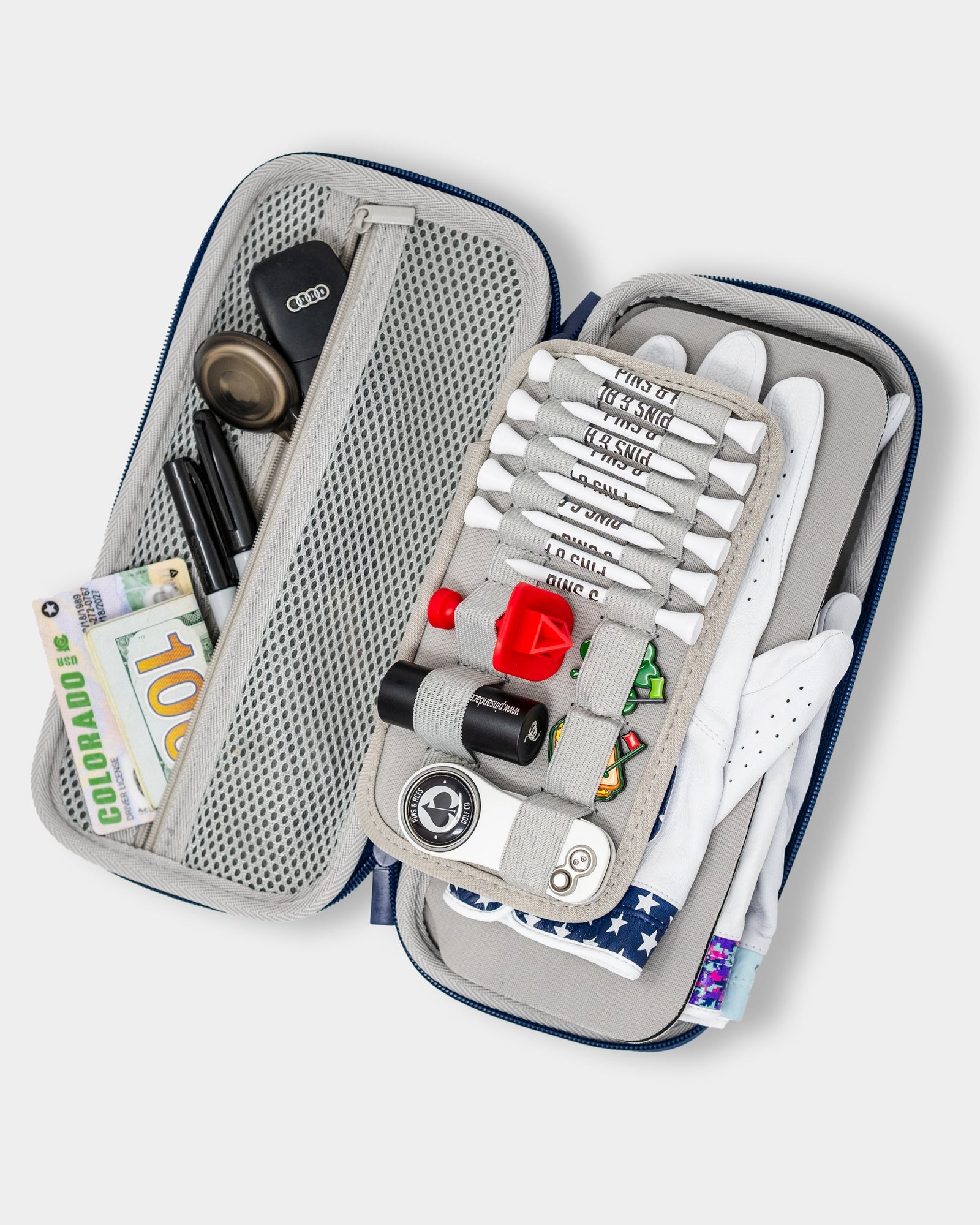 Open golf accessory caddy displaying organized compartments with white golf glove, multiple tees, ball markers, divot tool, and other golf essentials inside