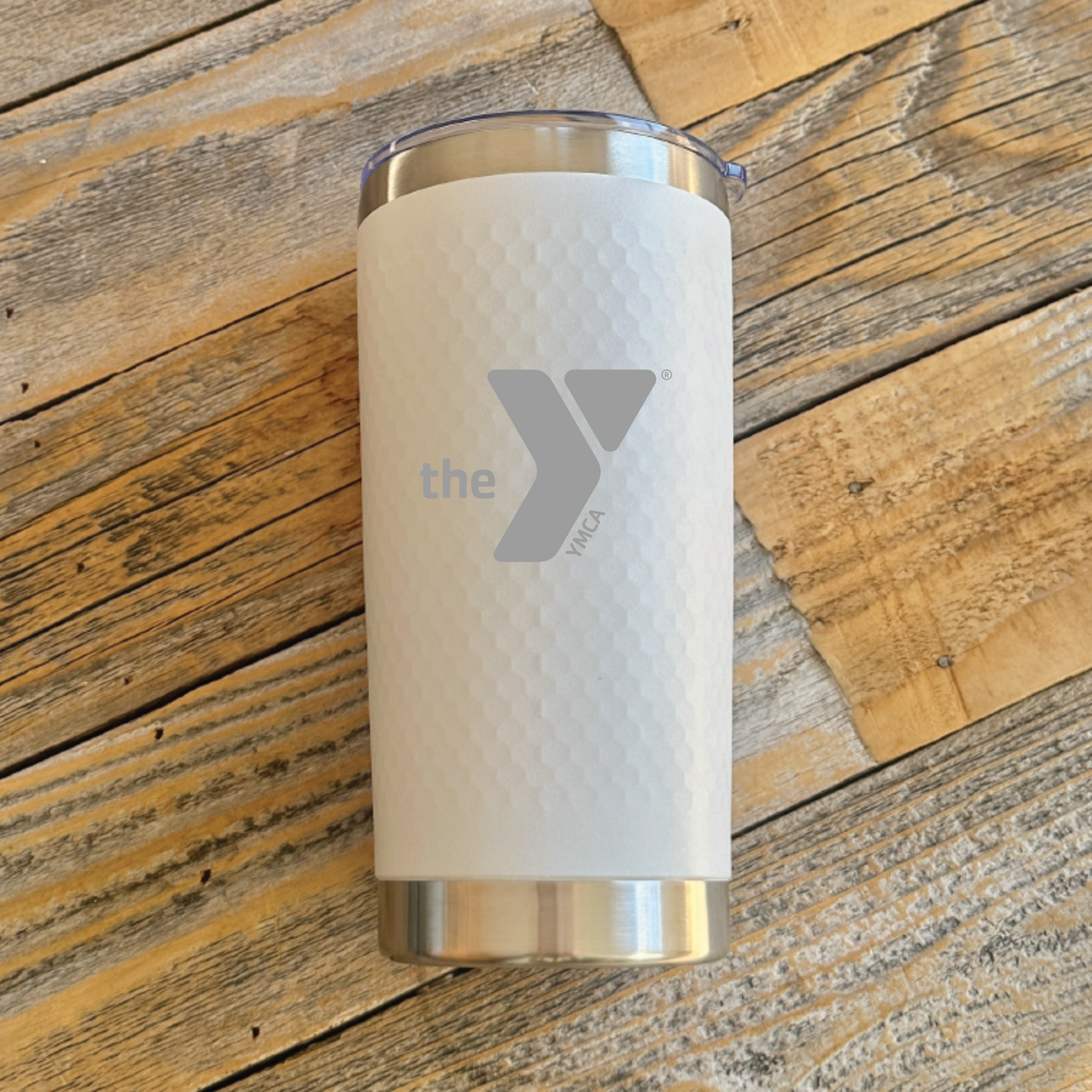 White insulated tumbler with stainless steel base and lid, featuring engraved logo and text on front, displayed on wooden surface