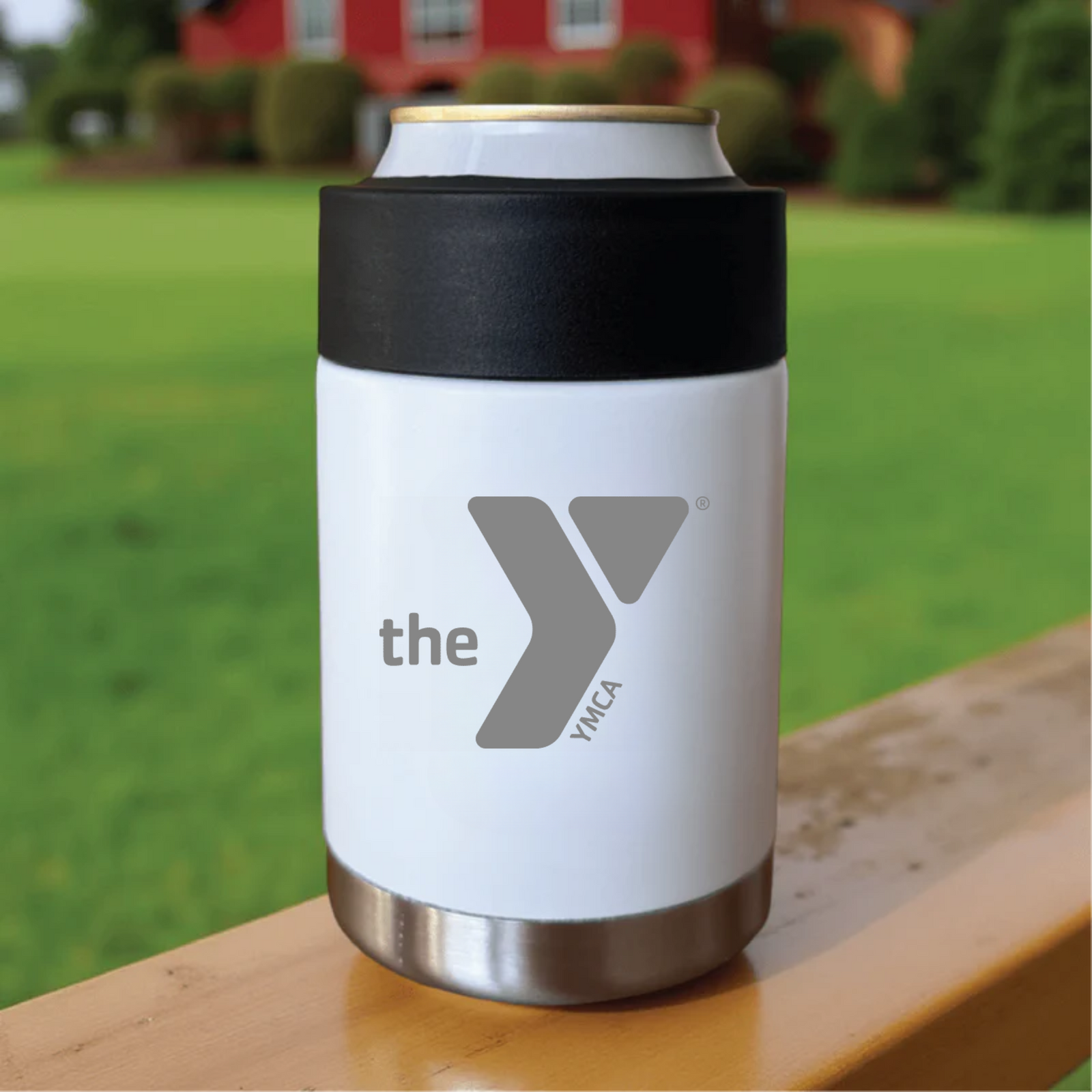 White insulated koozie with black neoprene band and gray logo, displayed on wooden surface with golf course background
