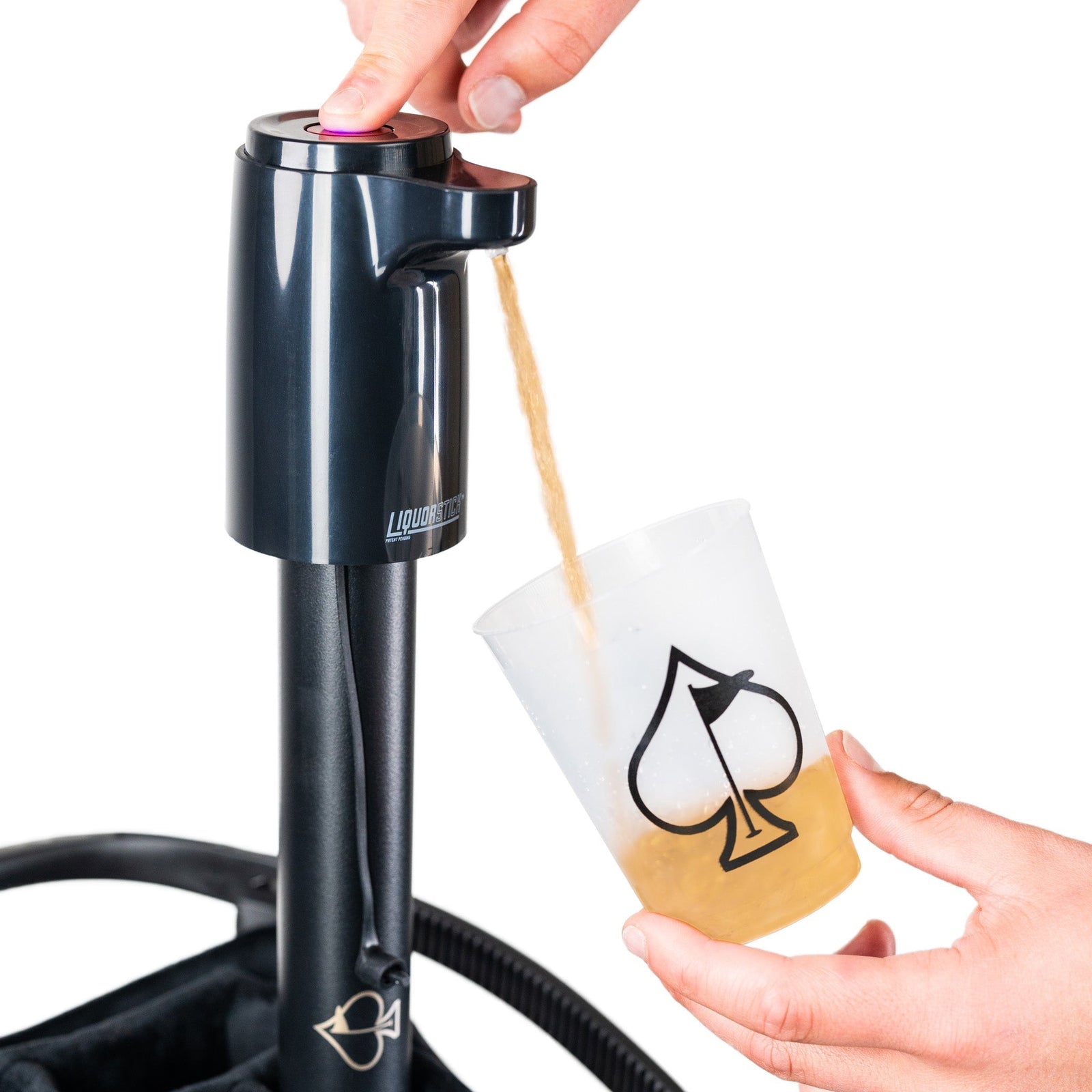 Black cylindrical beverage dispenser with pink button top being held above a white cup with spade symbol, pouring liquid from wooden tube spout.