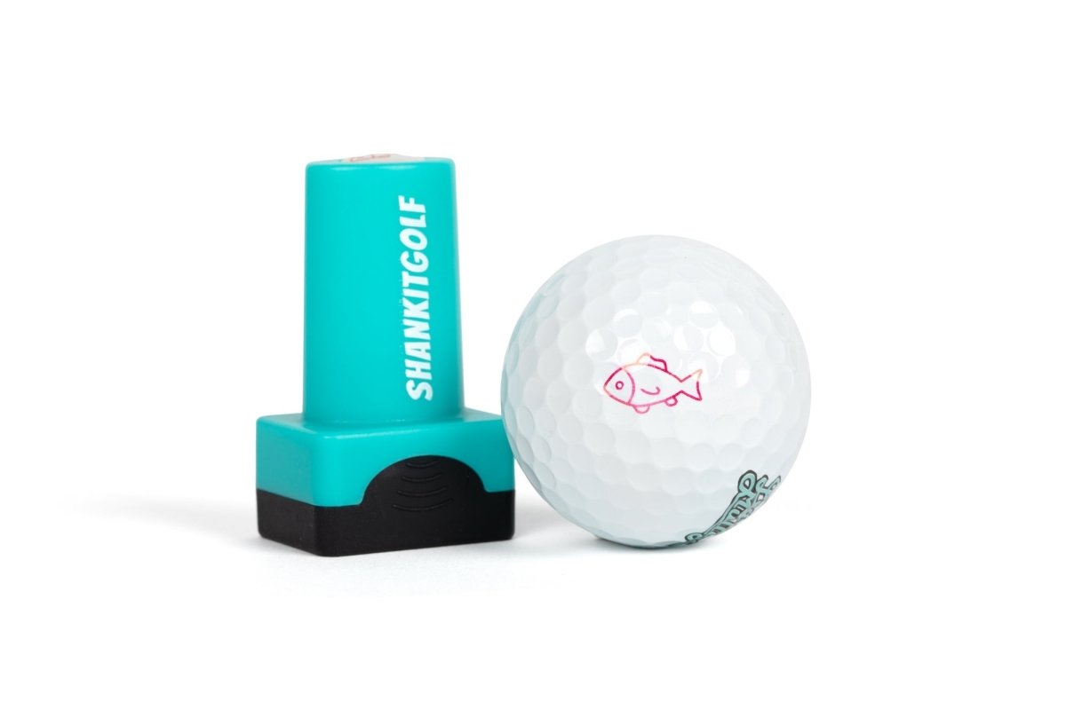 Turquoise ball stamper with white "SHANKITGOLF" text and black grip base displayed next to white golf ball stamped with pink fish design and teal text impression