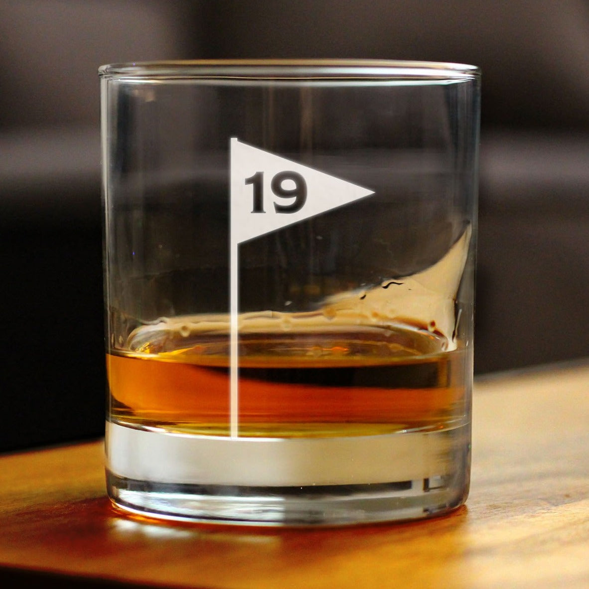 Rocks glass filled with amber liquid, engraved with golf flag design and sample number 19 in center