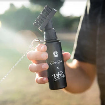 Black golf club brush with retractor clip held in hand, spraying water stream on club head during outdoor course use