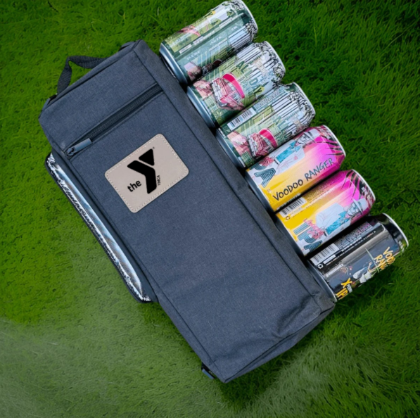 Navy insulated cooler bag filled with various beverage cans and bottles, displayed on green grass with handle and shoulder strap visible