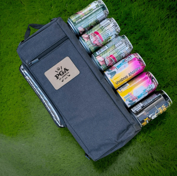 Navy insulated cooler bag displayed open on grass, revealing six cans and bottles inside, with branded logo patch visible on the exterior