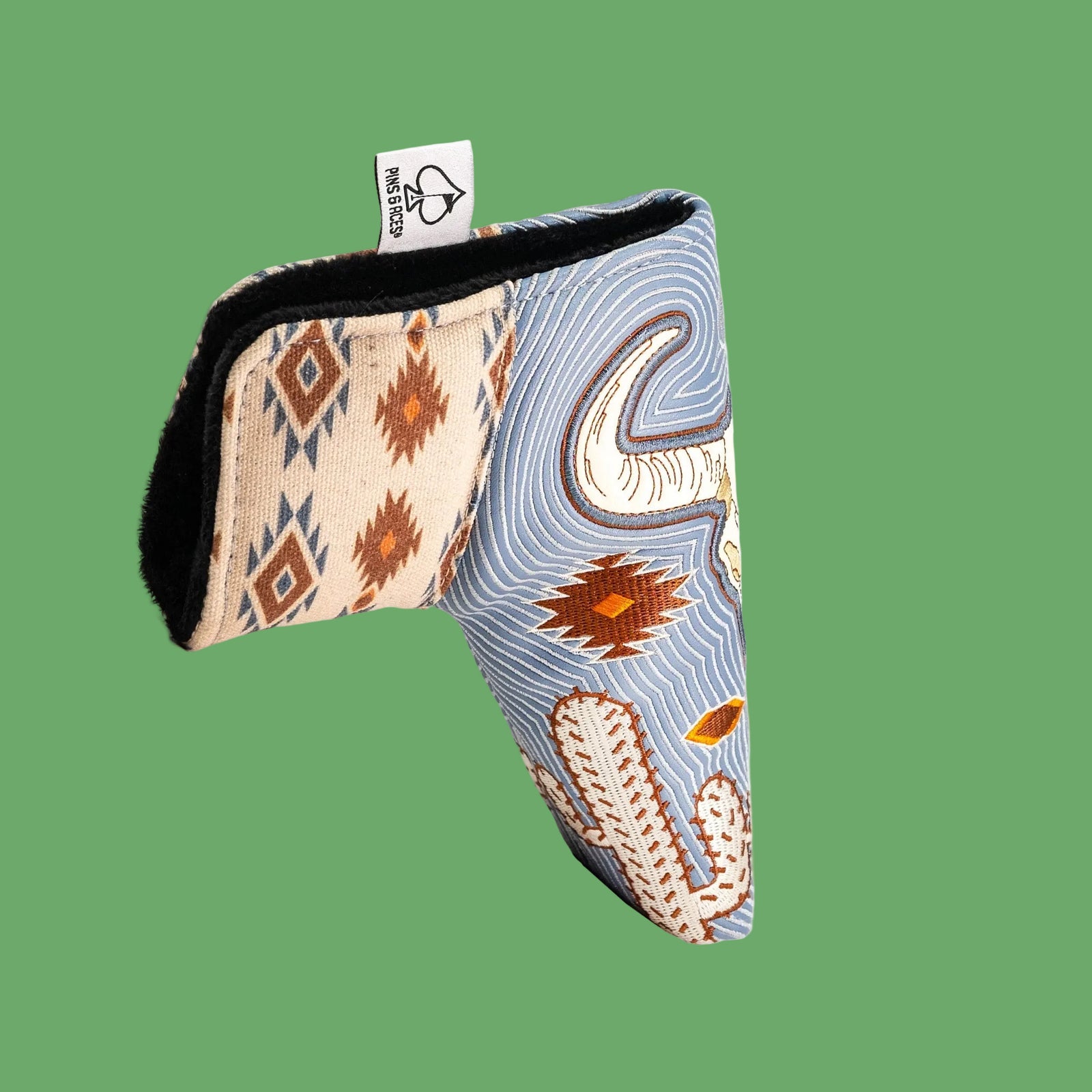 Putter blade cover with Southwestern-inspired patterns showing cream geometric design on back and blue striped front with cactus and bull skull motifs, black fleece interior visible