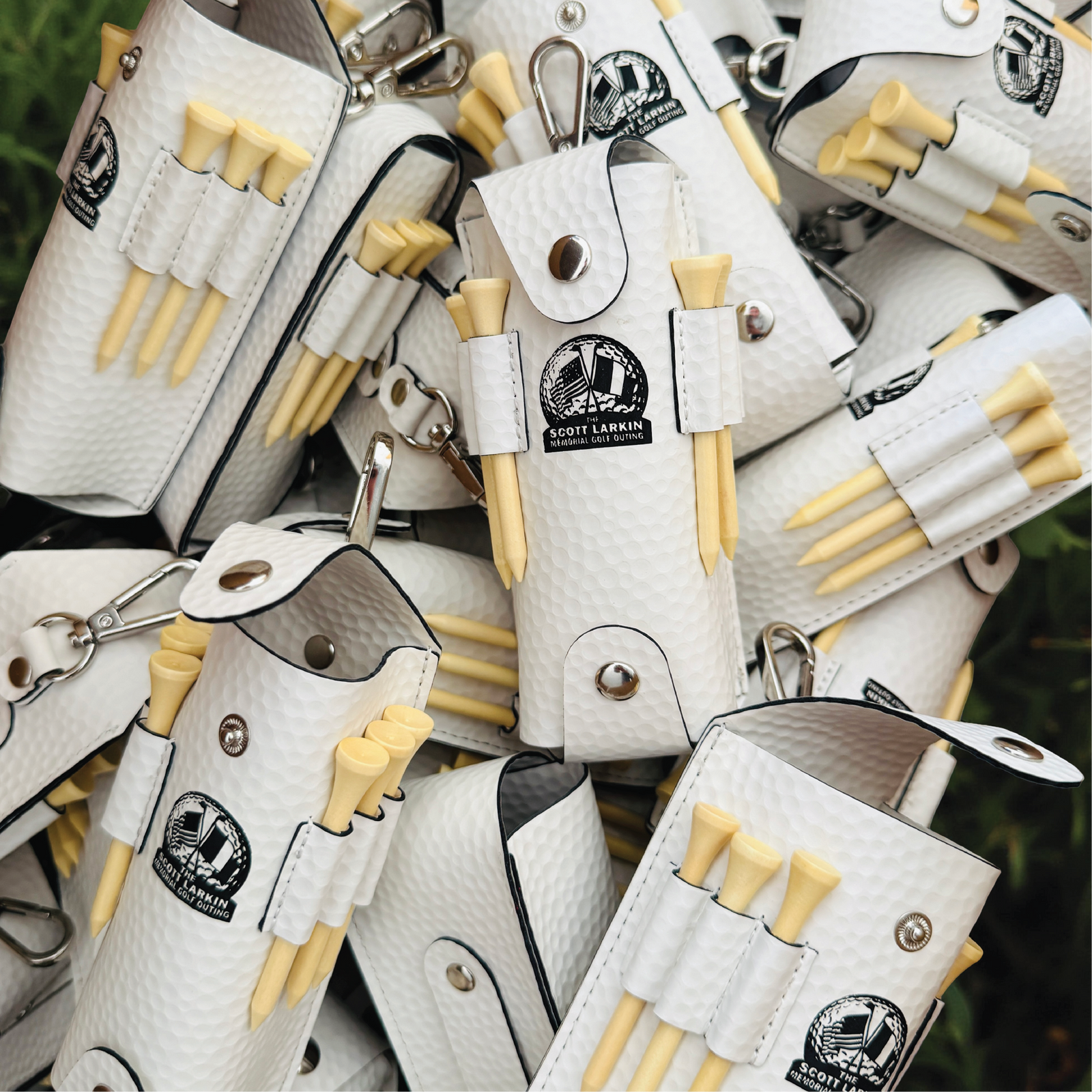 White textured golf ball pouches with wooden tees and carabiner clips, displaying logo printing on multiple units arranged overhead