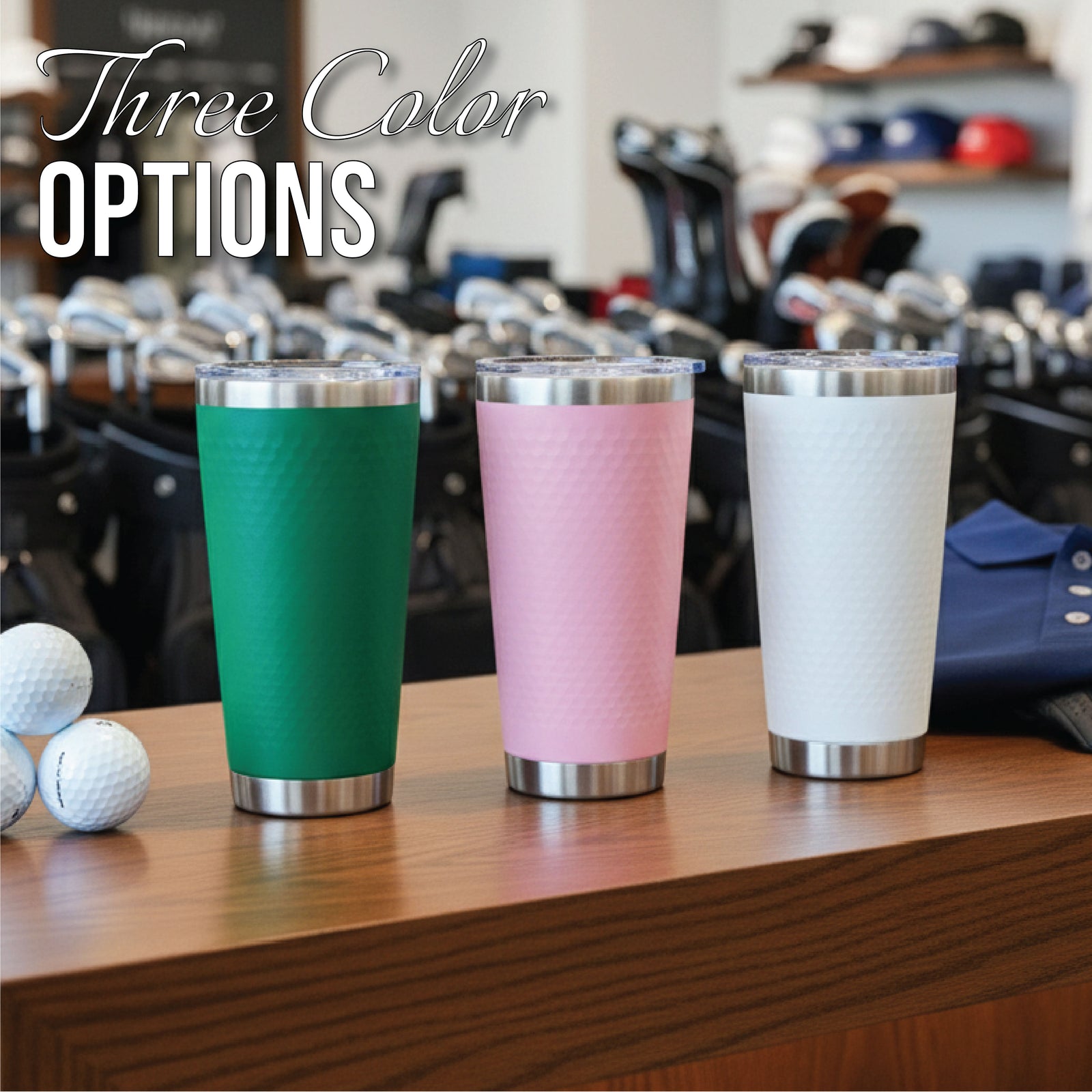 Three insulated tumblers in green, pink, and white with stainless steel bands, displayed on wooden surface with golf balls and golf equipment in background