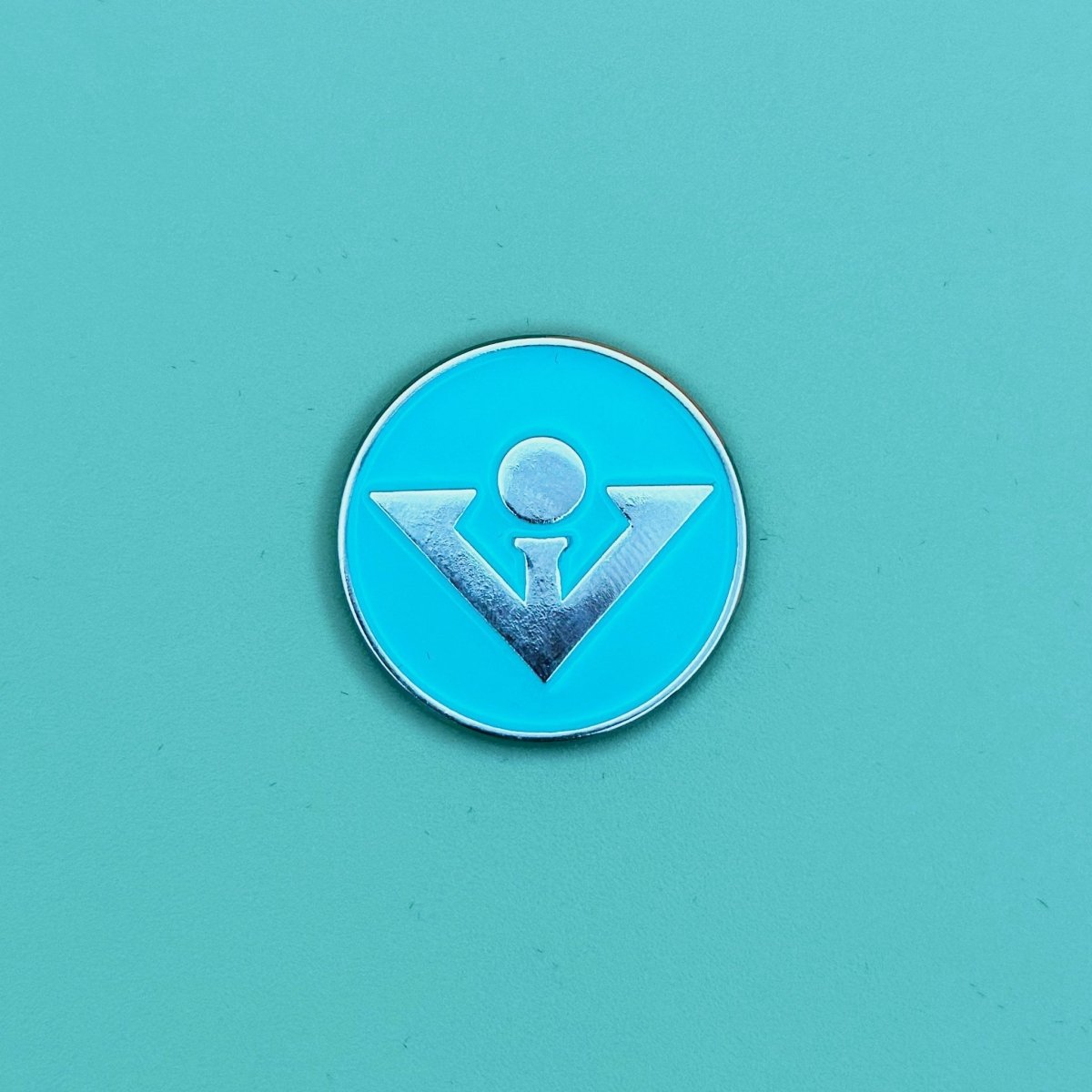 Bright turquoise circular ball marker with silver divot tool icon and metallic silver rim, centered on matching turquoise background
