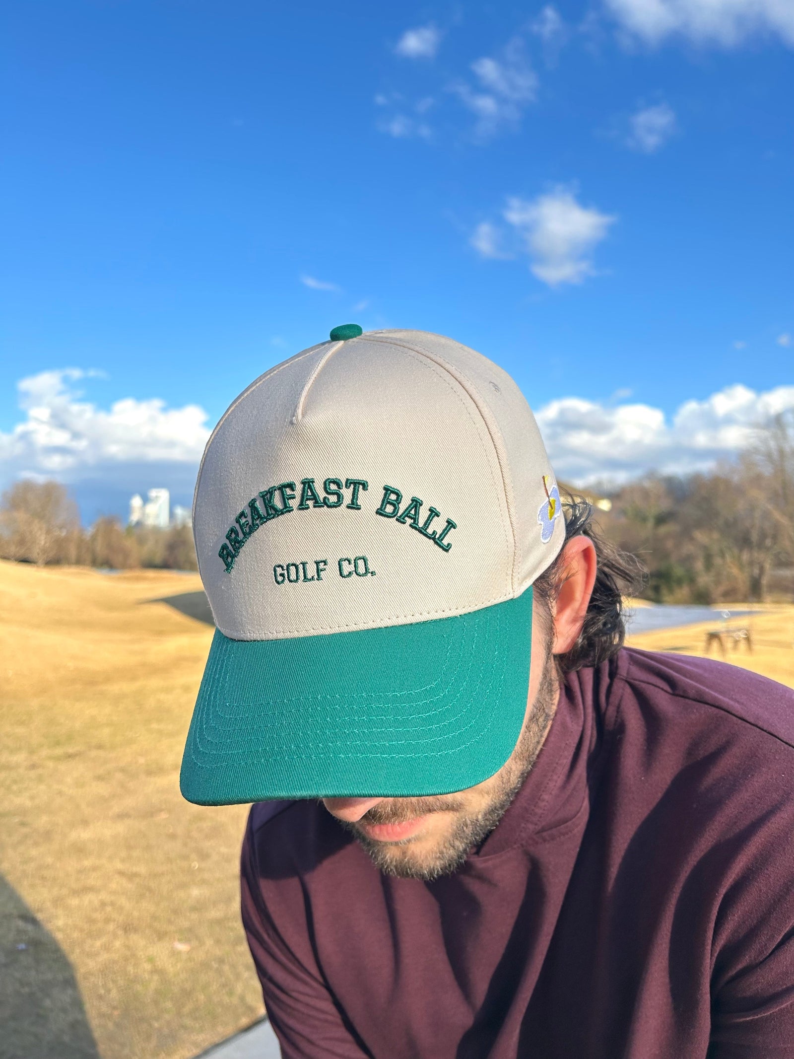 Person wearing a cap with 'Breakfast Ball Golf Co.' text on a golf course