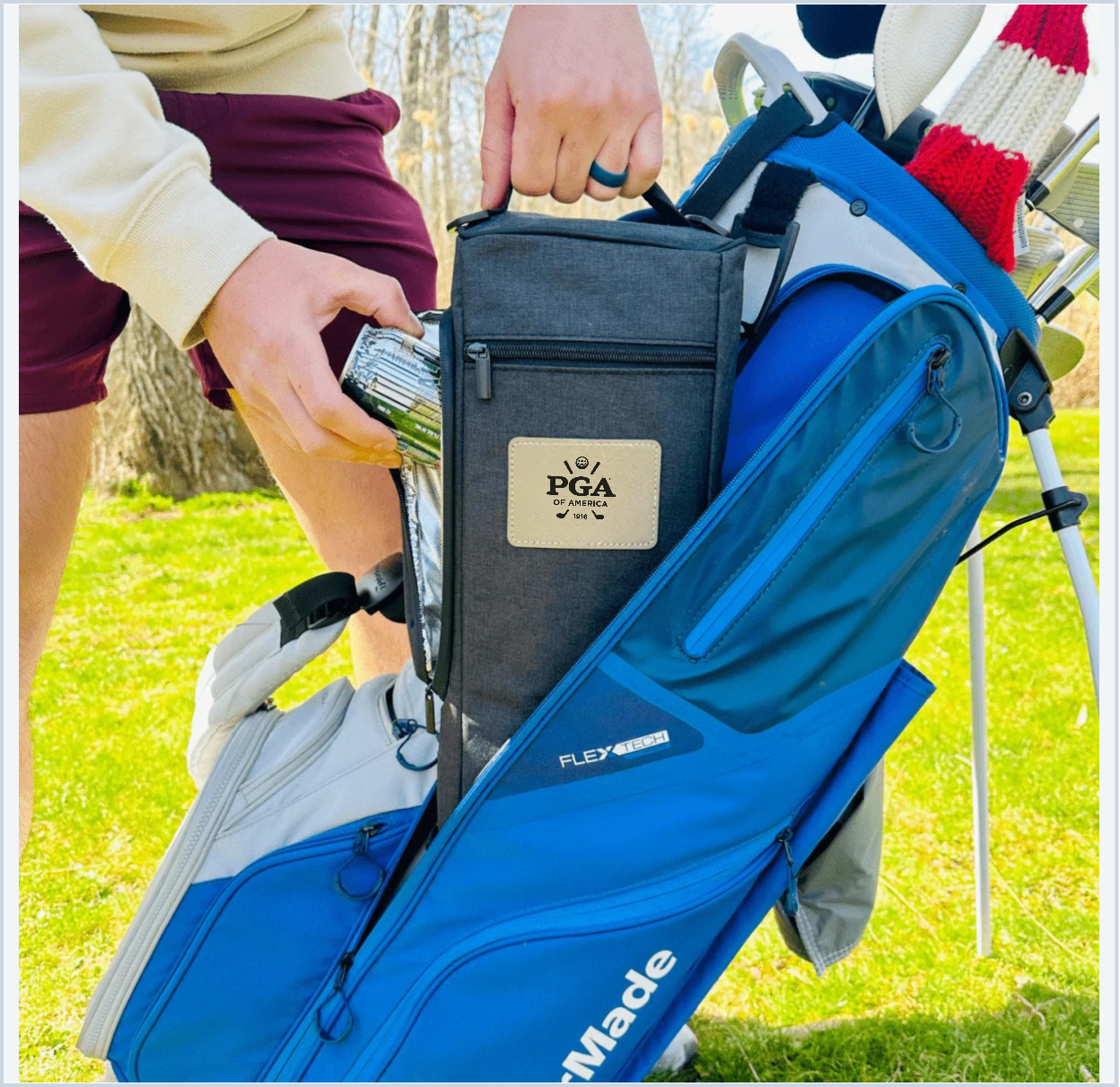 Charcoal insulated cooler bag with leather patch logo being placed into blue golf bag during on-course use, showing size and functionality with golfers in background.