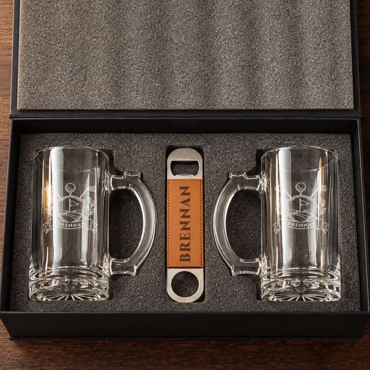 Golf beer mug gift set open in its foam-lined box: two glass beer mugs etched with a golf crest and BRENNAN, plus an engraved bottle opener