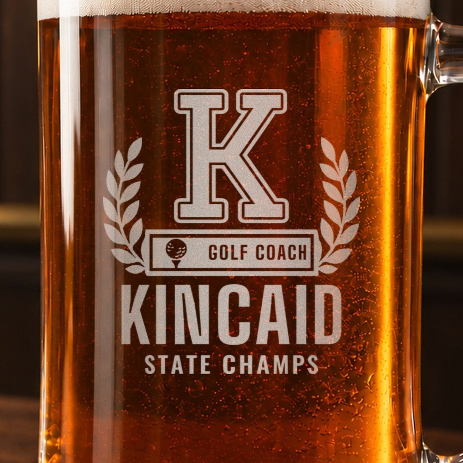 Close-up of a golf coach beer stein engraving, varsity K in a laurel wreath, GOLF COACH bar, KINCAID and STATE CHAMPS, through amber beer