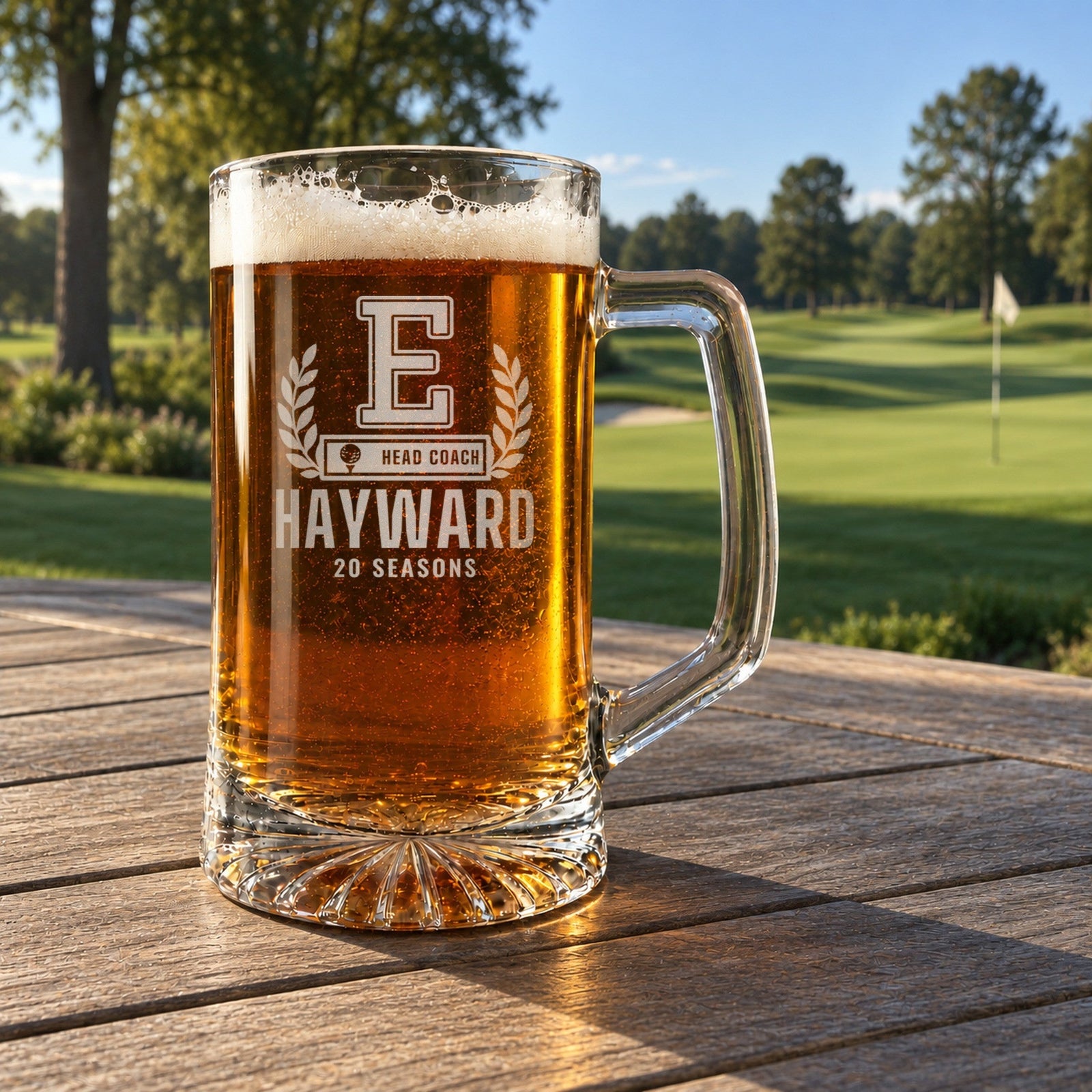 Varsity letter golf coach beer stein engraved E, HAYWARD and 20 SEASONS on a wooden rail overlooking a golf course in afternoon light