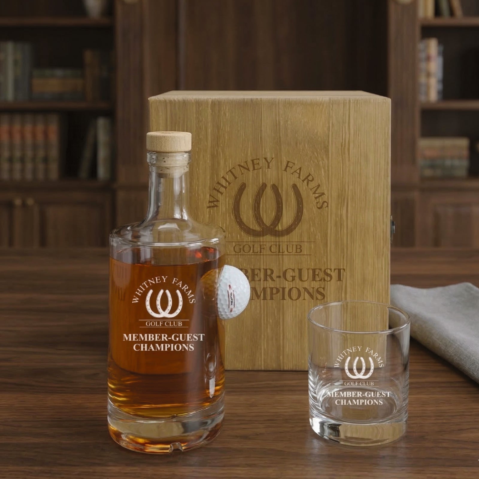 Wooden gift box engraved with "Whitney Farms Golf Club Member-Guest Champions" logo, displayed with matching decanter bottle containing amber liquid and coordinating rocks glass