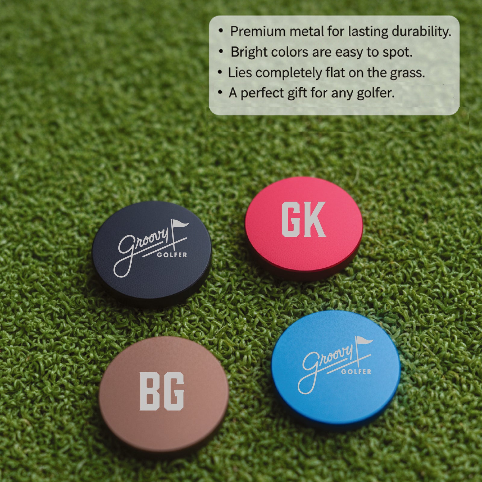 Four metal ball markers on artificial green turf showing sample personalizations including initials "BG" and "GK" engraved on colored surfaces