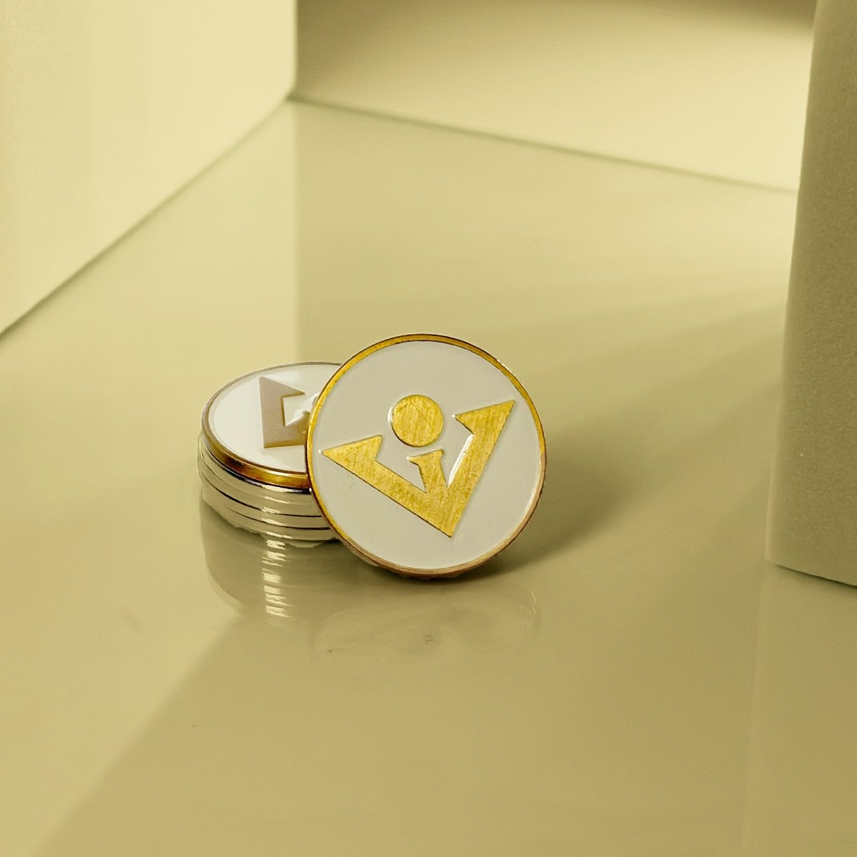 Cream and gold golf ball marker with magnetic backing, displayed open to show stacked interior discs and gold geometric design on white surface