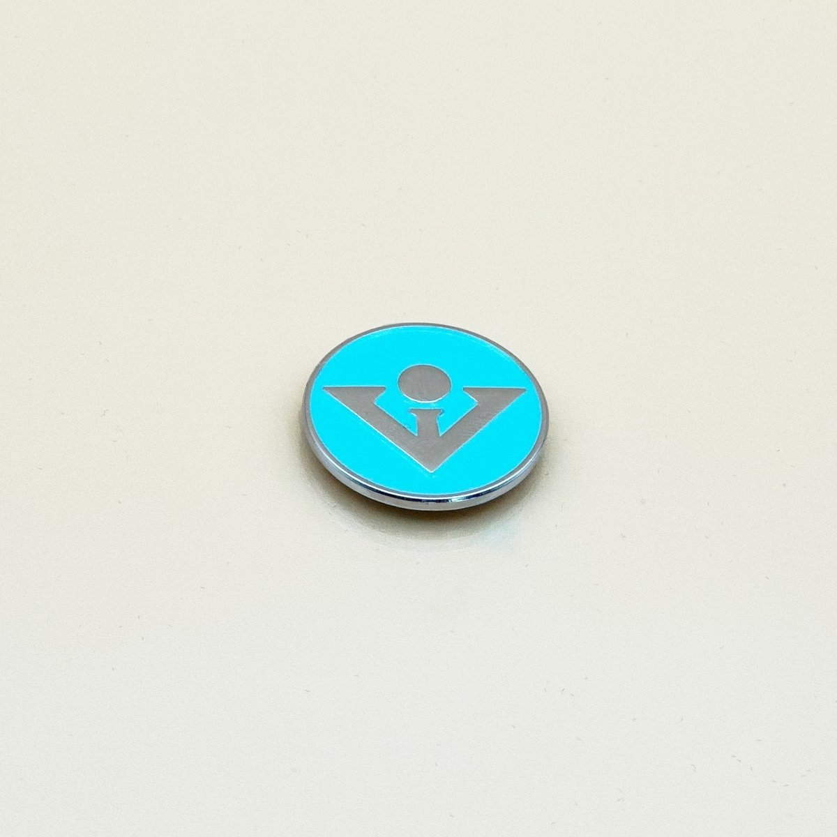 Bright turquoise circular ball marker with silver metallic logo design and chrome rim, displayed against neutral background