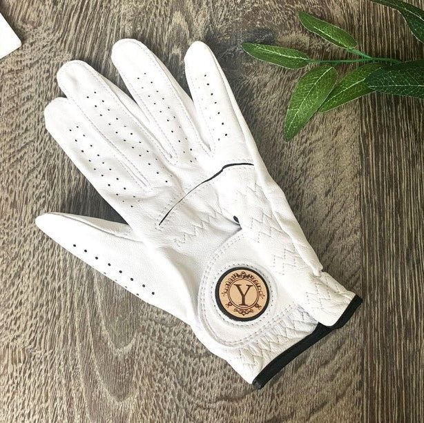 White leather golf glove with perforated ventilation holes and a wooden ball marker disc with sample initial "Y" on the thumb side.
