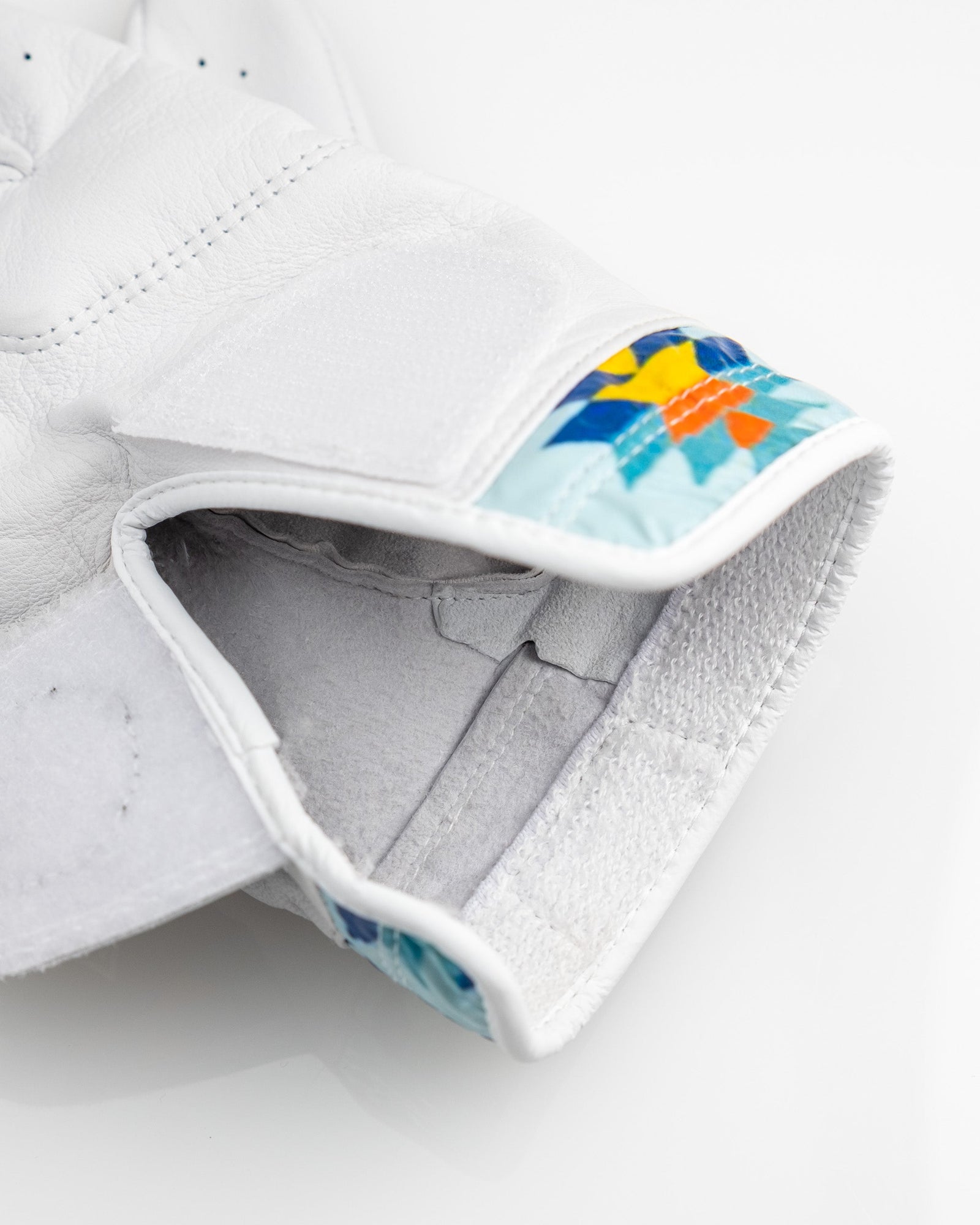 White leather golf glove with colorful geometric Southwest pattern on cuff, interior view showing gray moisture-wicking lining and stitched seams
