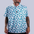 Men’s white polo with emerald-green four-leaf clover print – breathable, stretch-fit, and performance-ready.
