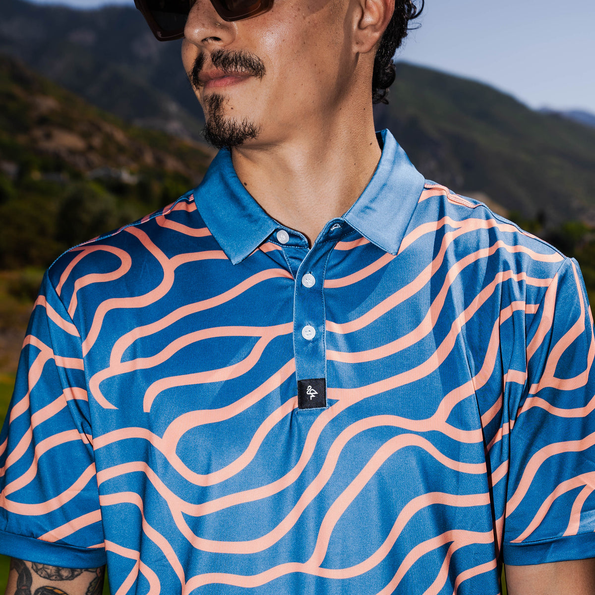 Men’s navy polo with peach wave-pattern print – dynamic, breathable, stretch-performance ready.