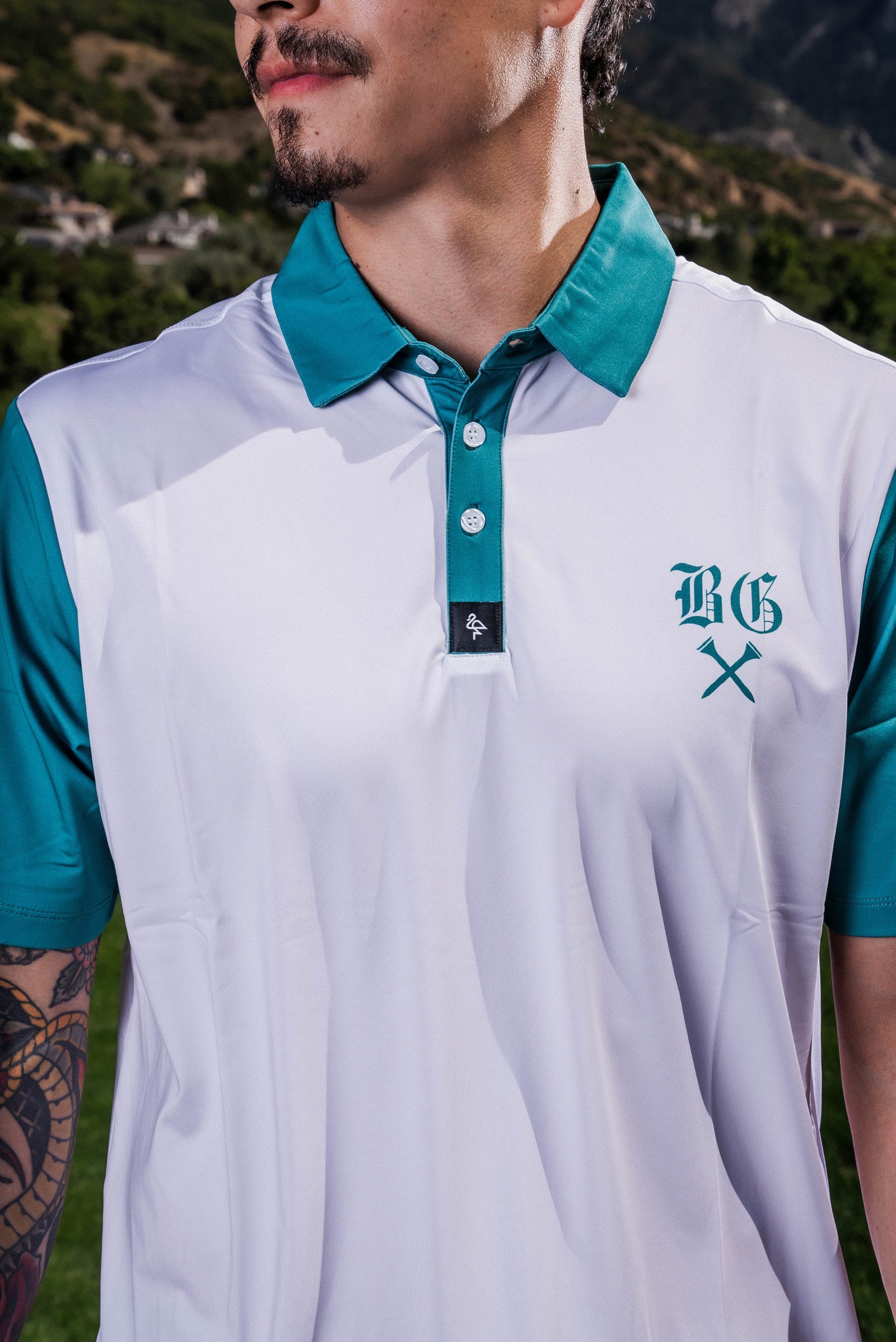 Men's white polo with green BG logo print – breathable, stretch fit with moisture control and wrinkle resistance.