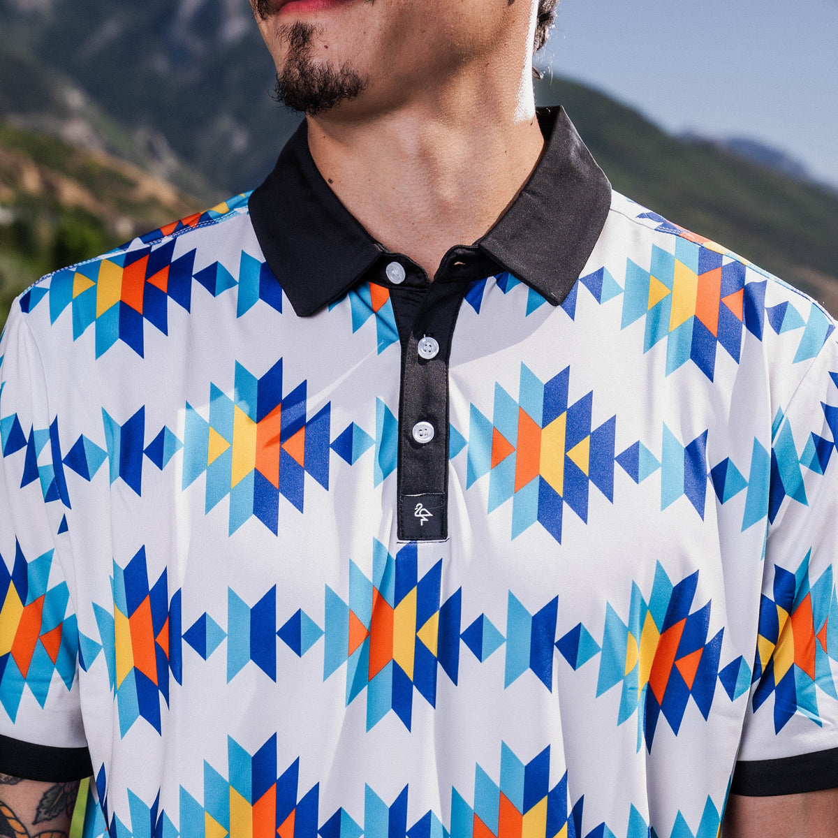 White Aztec polo with teal, orange &amp; navy diamond pattern, 4‑way stretch, UPF 50+, moisture‑wicking, anti‑odor &amp; wrinkle resistance.