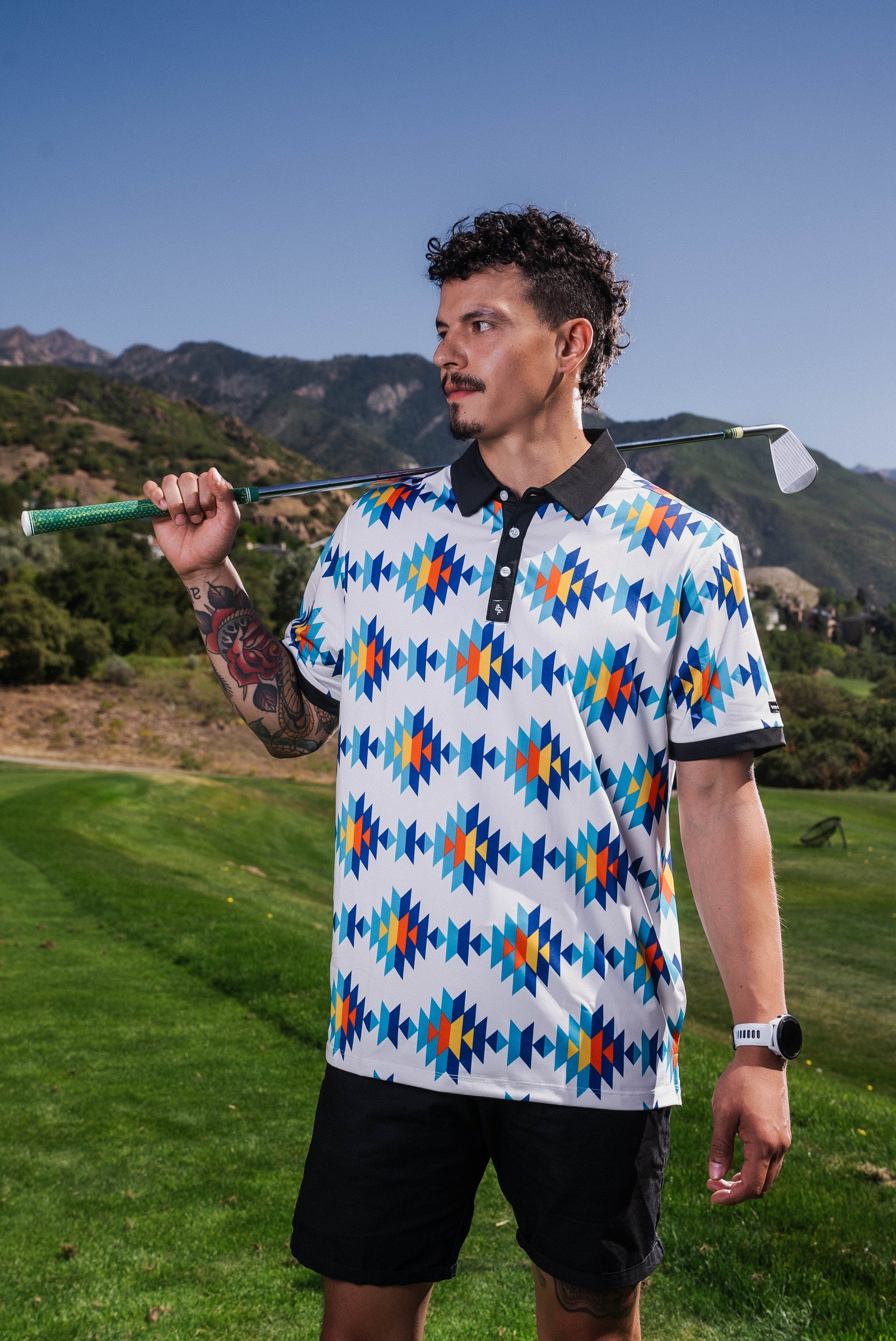 White Aztec polo with teal, orange & navy diamond pattern, 4‑way stretch, UPF 50+, moisture‑wicking, anti‑odor & wrinkle resistance.