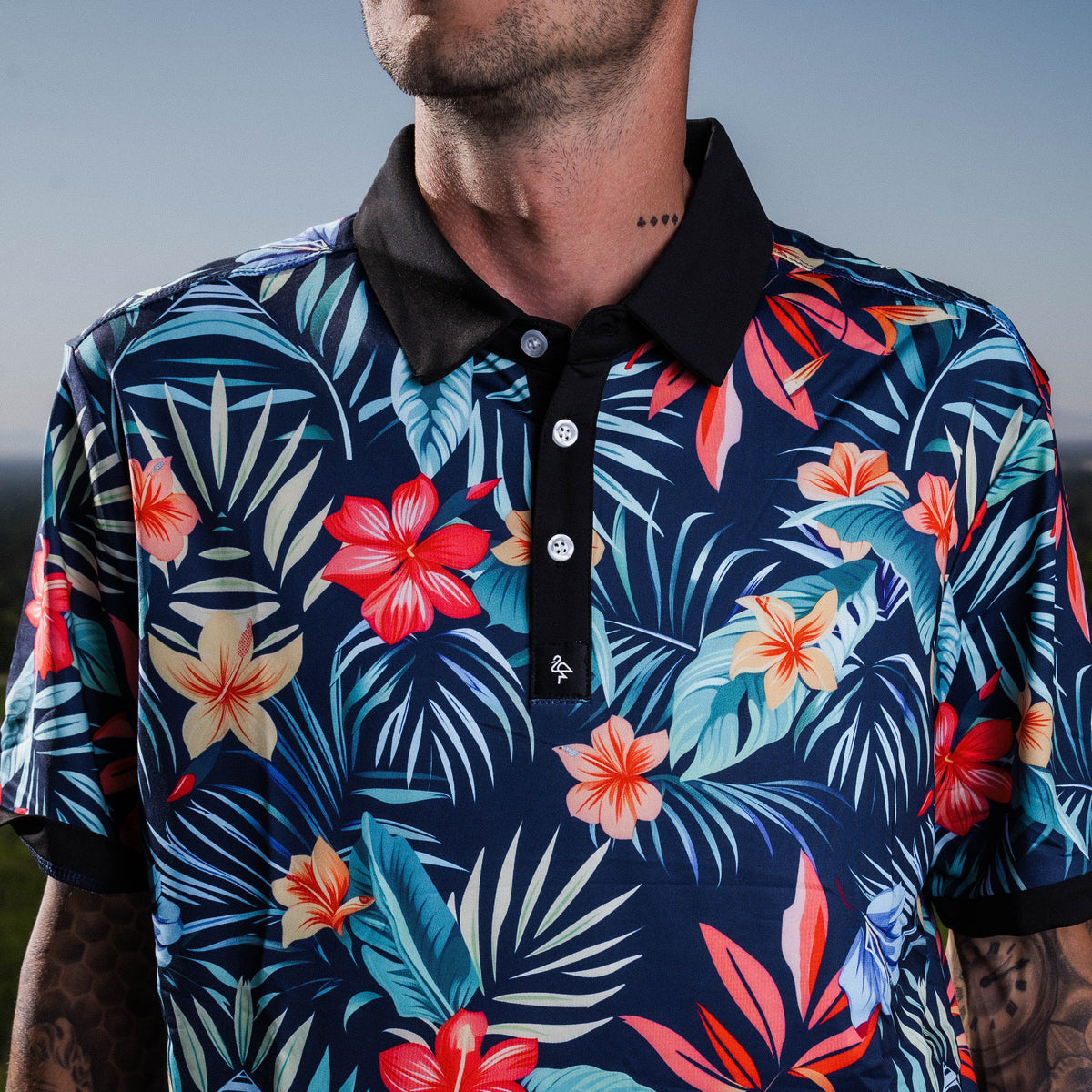 Men’s navy polo with bold coral and teal tropical floral print – vibrant, breathable, performance-ready.
