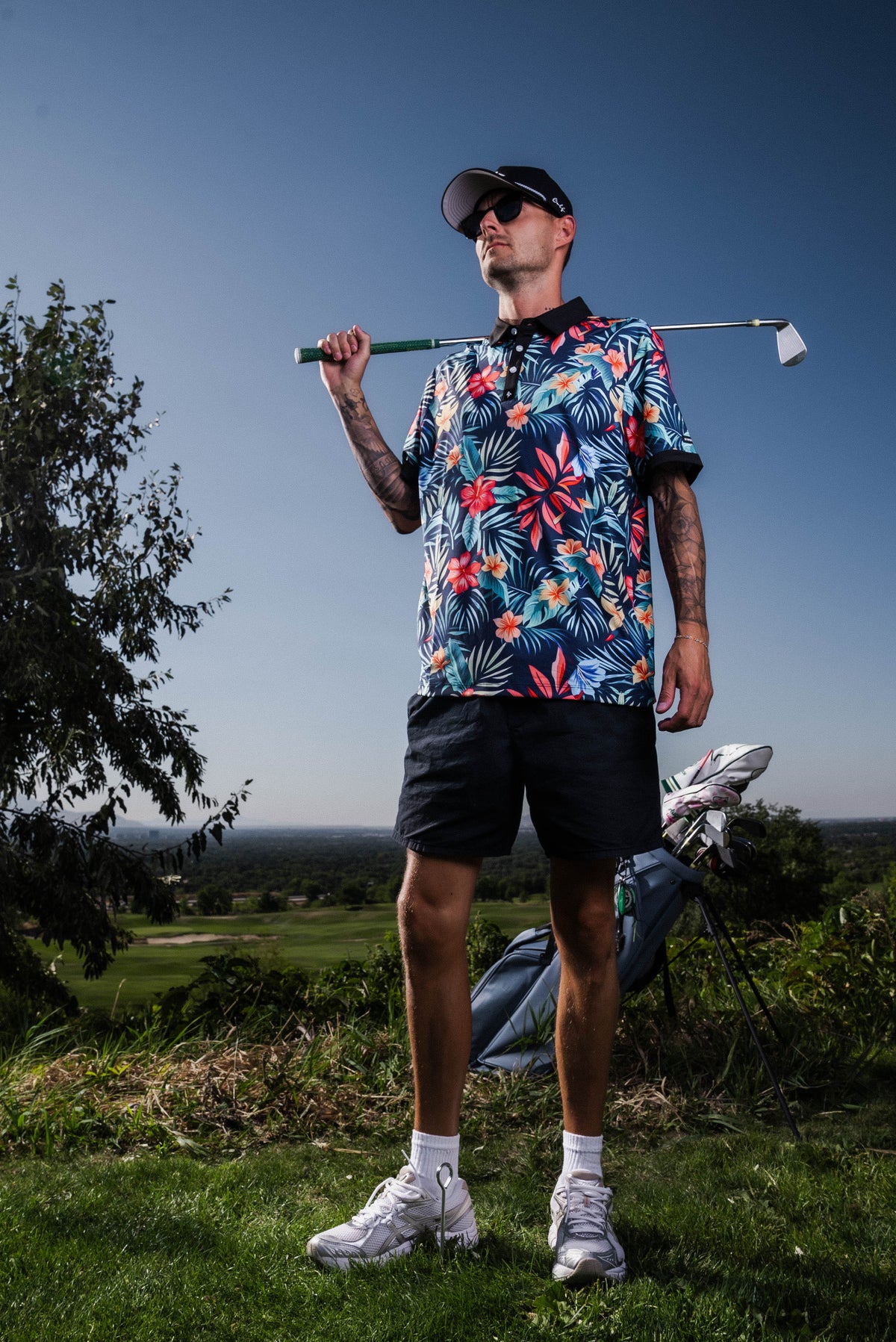 Men’s navy polo with bold coral and teal tropical floral print – vibrant, breathable, performance-ready.