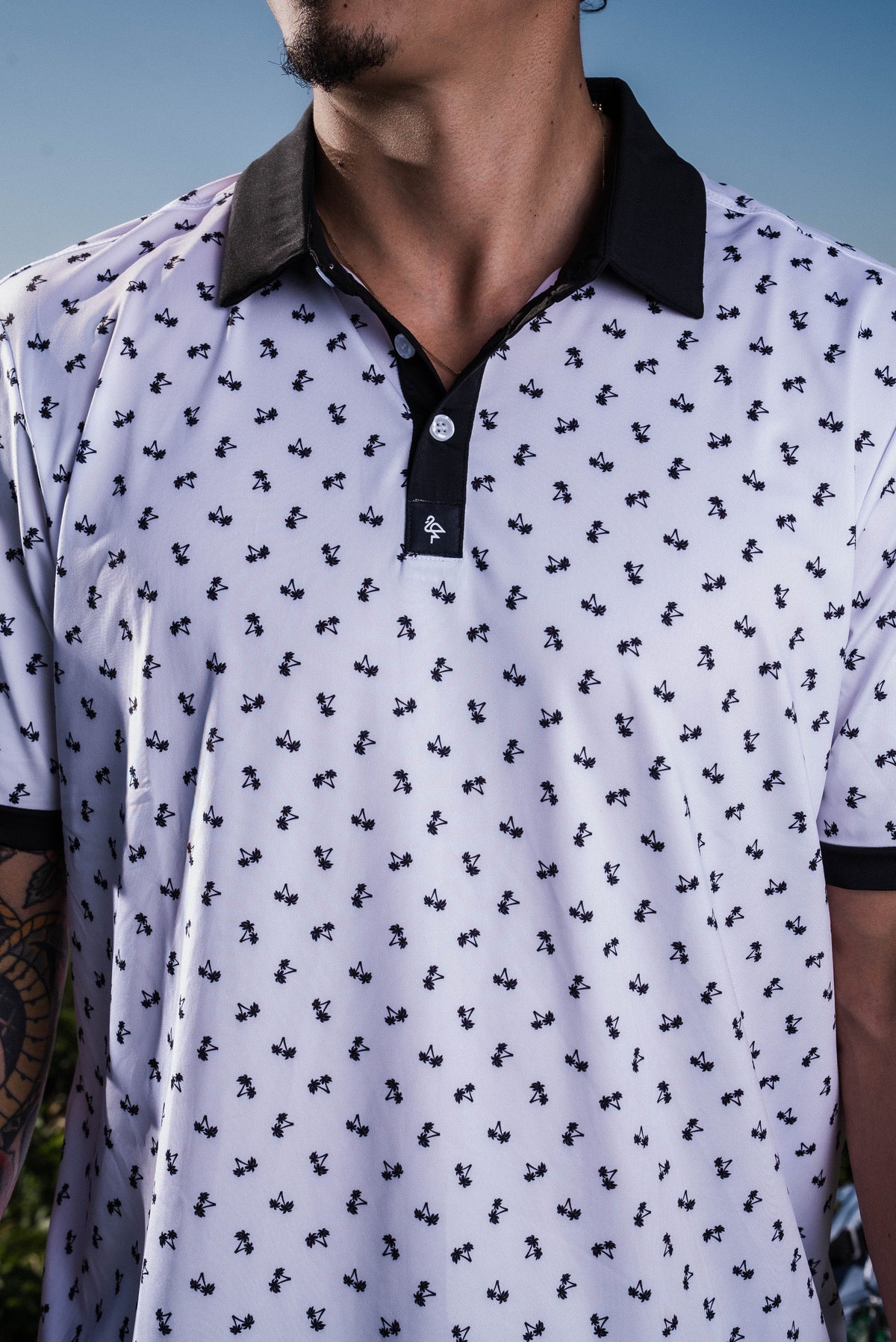 Men’s white polo with small navy palm leaf print and contrast collar – tropical-infused, stretch-performance ready.
