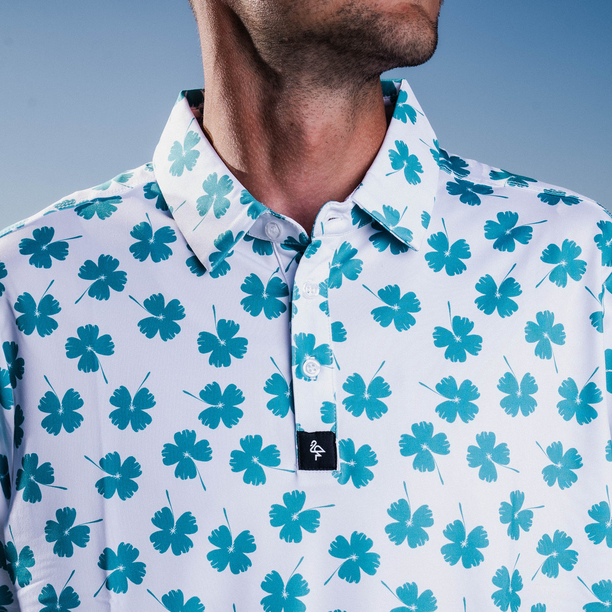 Men’s white polo with emerald-green four-leaf clover print – breathable, stretch-fit, and performance-ready.