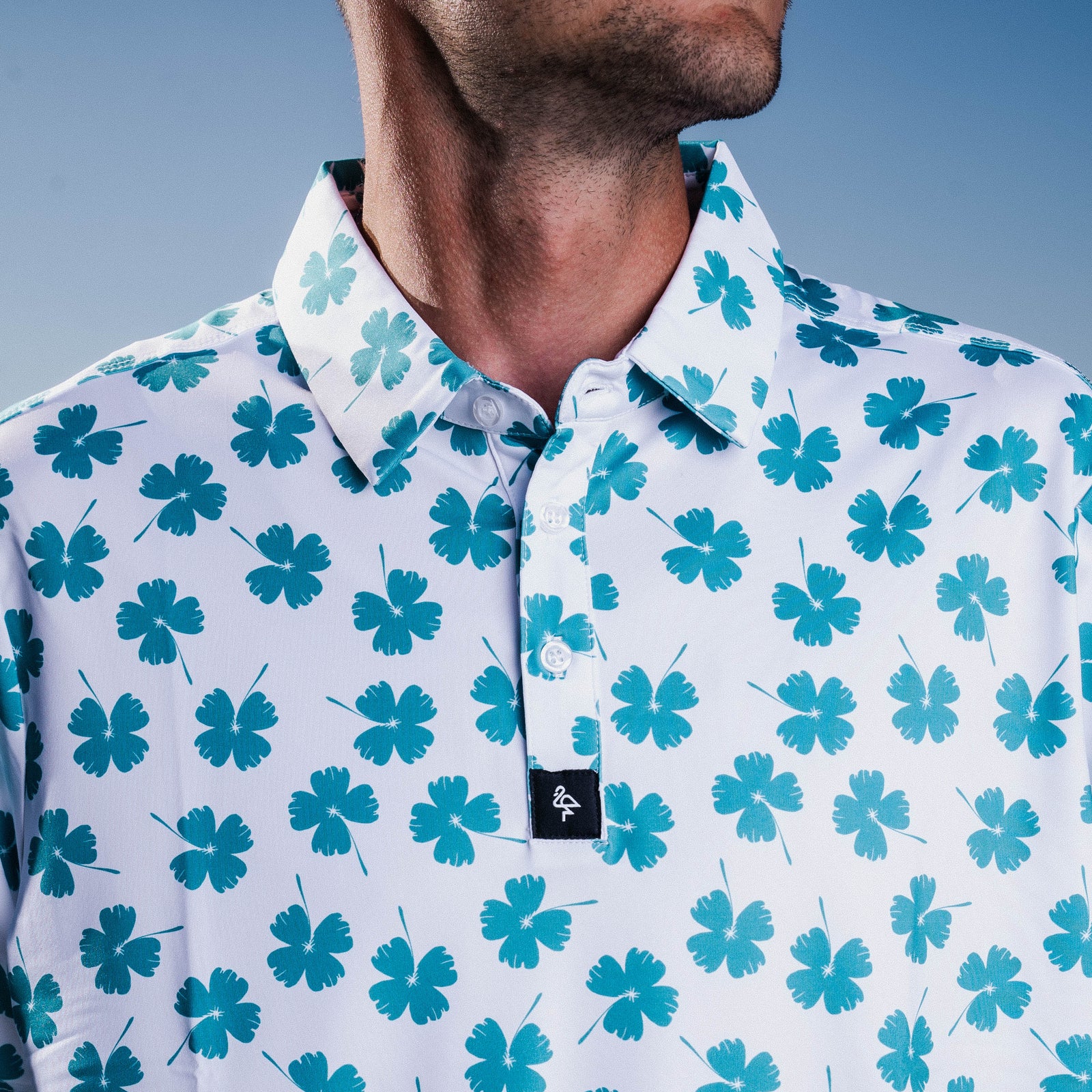 Men’s white polo with emerald-green four-leaf clover print – breathable, stretch-fit, and performance-ready.