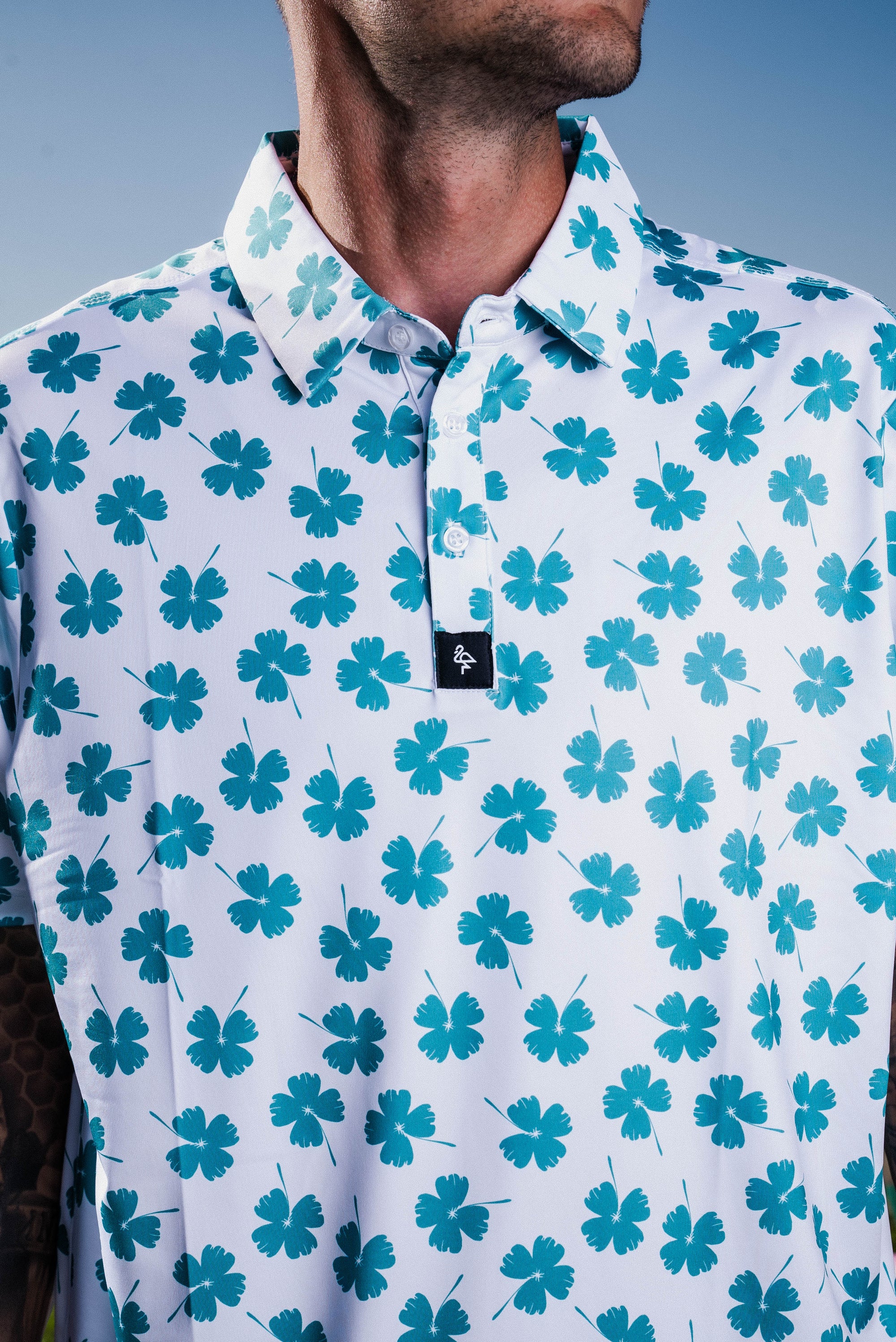 Men’s white polo with emerald-green four-leaf clover print – breathable, stretch-fit, and performance-ready.