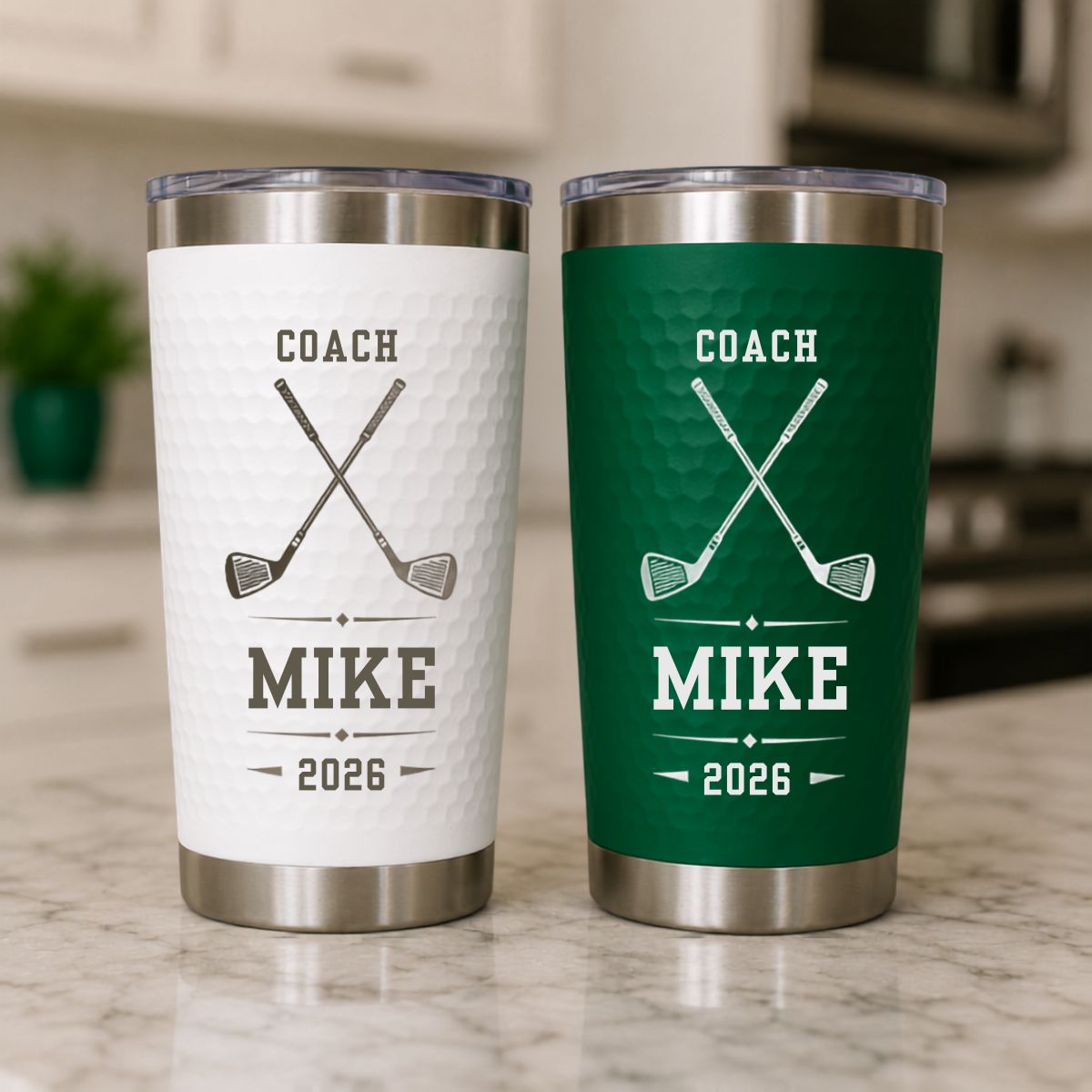 Golf coach gift tumblers in white and green, each engraved COACH with crossed golf clubs, MIKE and 2026, side by side on a kitchen counter