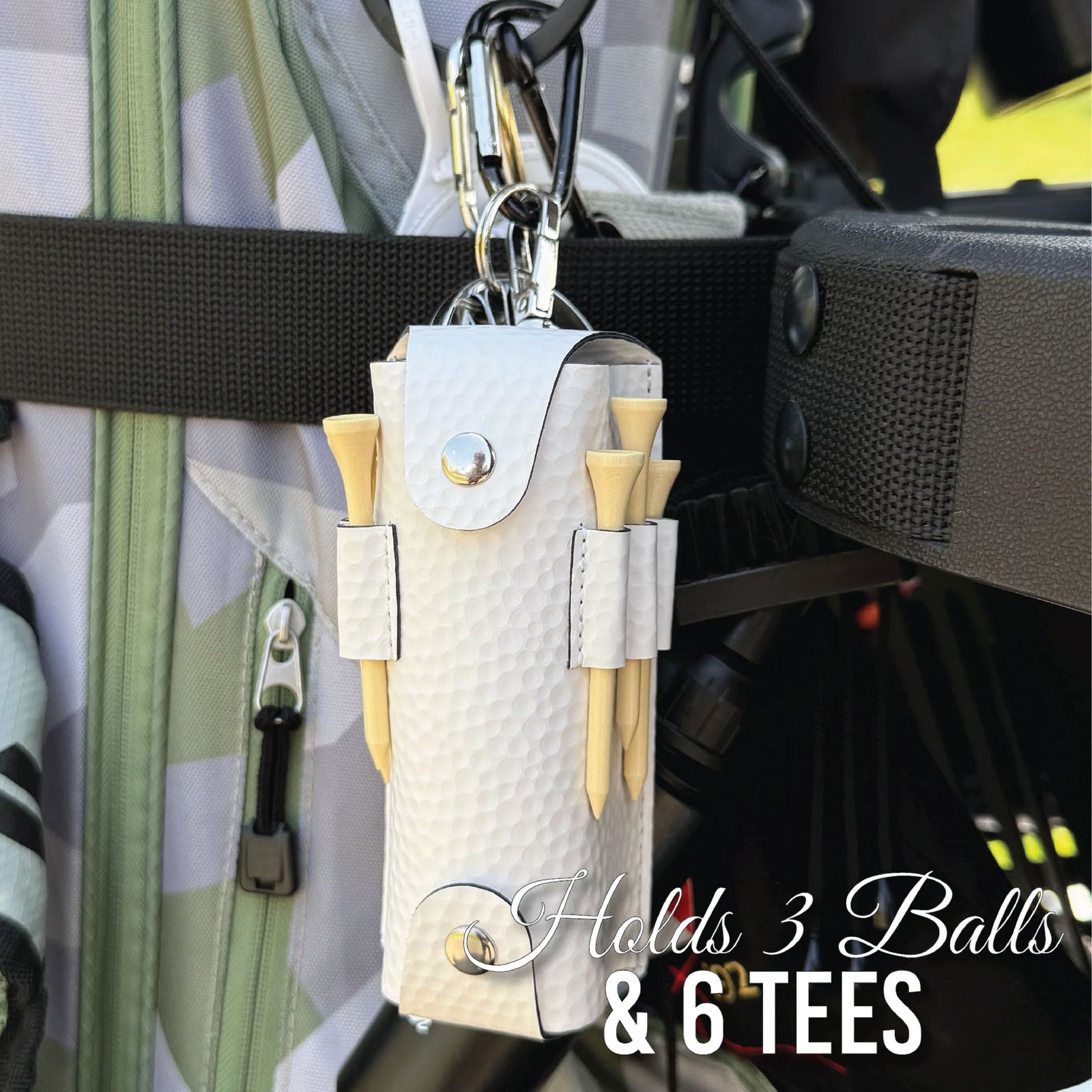 White golf ball and tee holder attached to golf bag with carabiner clip, holding three golf balls and six wooden tees