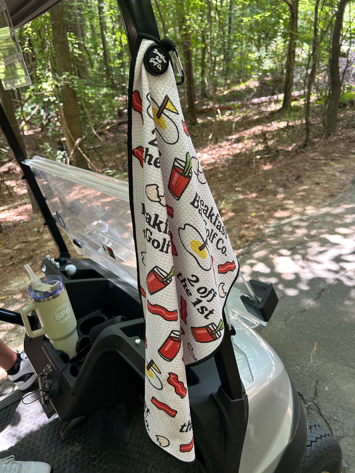 Golf towel with colorful designs hanging from a golf cart in a wooded area