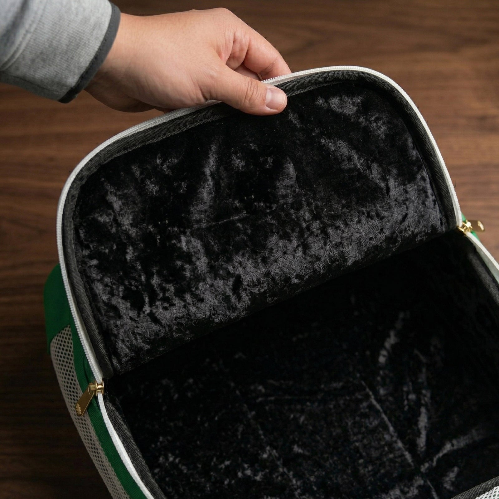 Green golf shoe bag with soft black plush interior lining, held open to show ventilated storage space, with gold zipper detail visible.