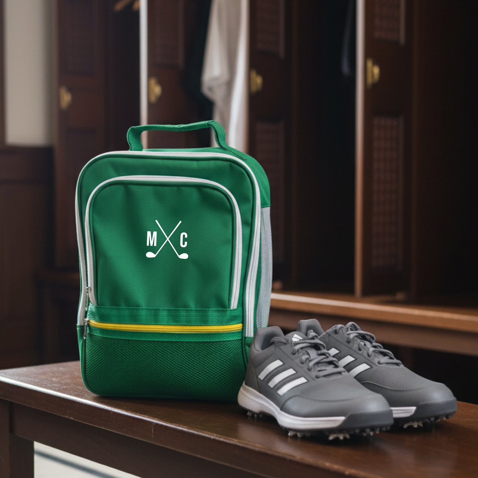 Green golf shoe bag embroidered with sample initials "MC" and crossed clubs, displayed with gray and white golf shoes on wooden table
