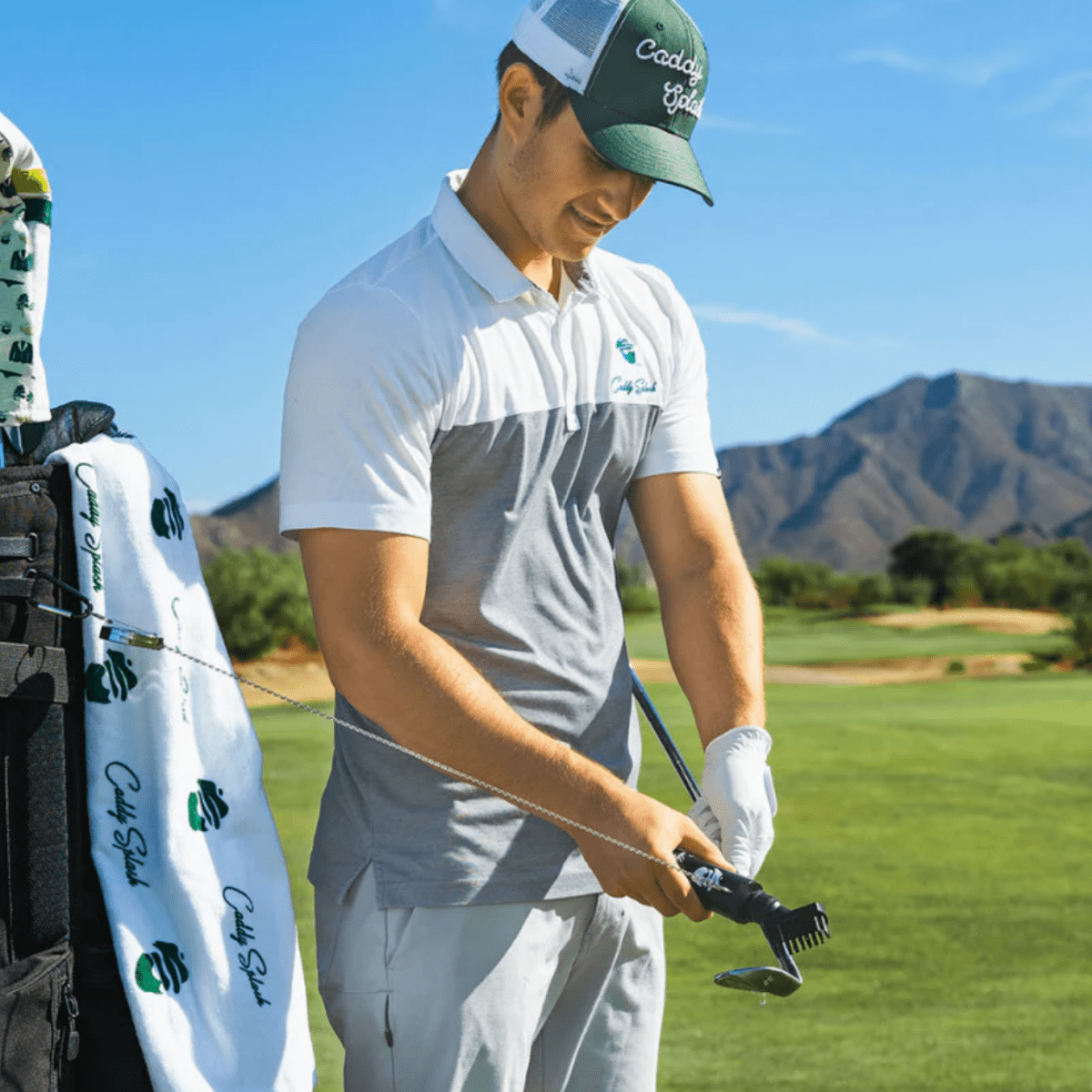 Golfer on course holding divot tool with sample personalized name engraved on white golf towel attached to bag