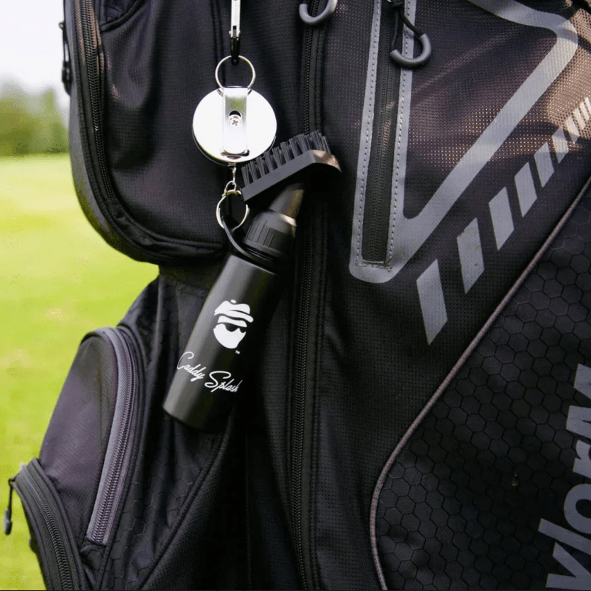 Black golf flask with sample engraving "Caddy Spliced" attached to golf bag with white carabiner and keychain clip on course