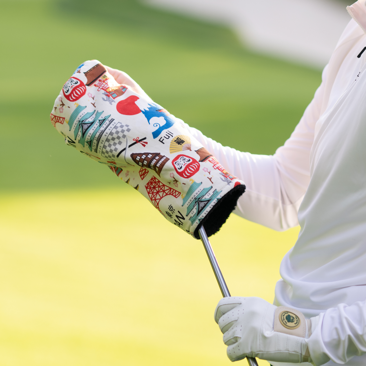 Handmade Tokyo-themed driver head cover with embroidered buildings, lanterns, and cultural icons in red, blue, and cream on white fabric, shown on golf club in use.