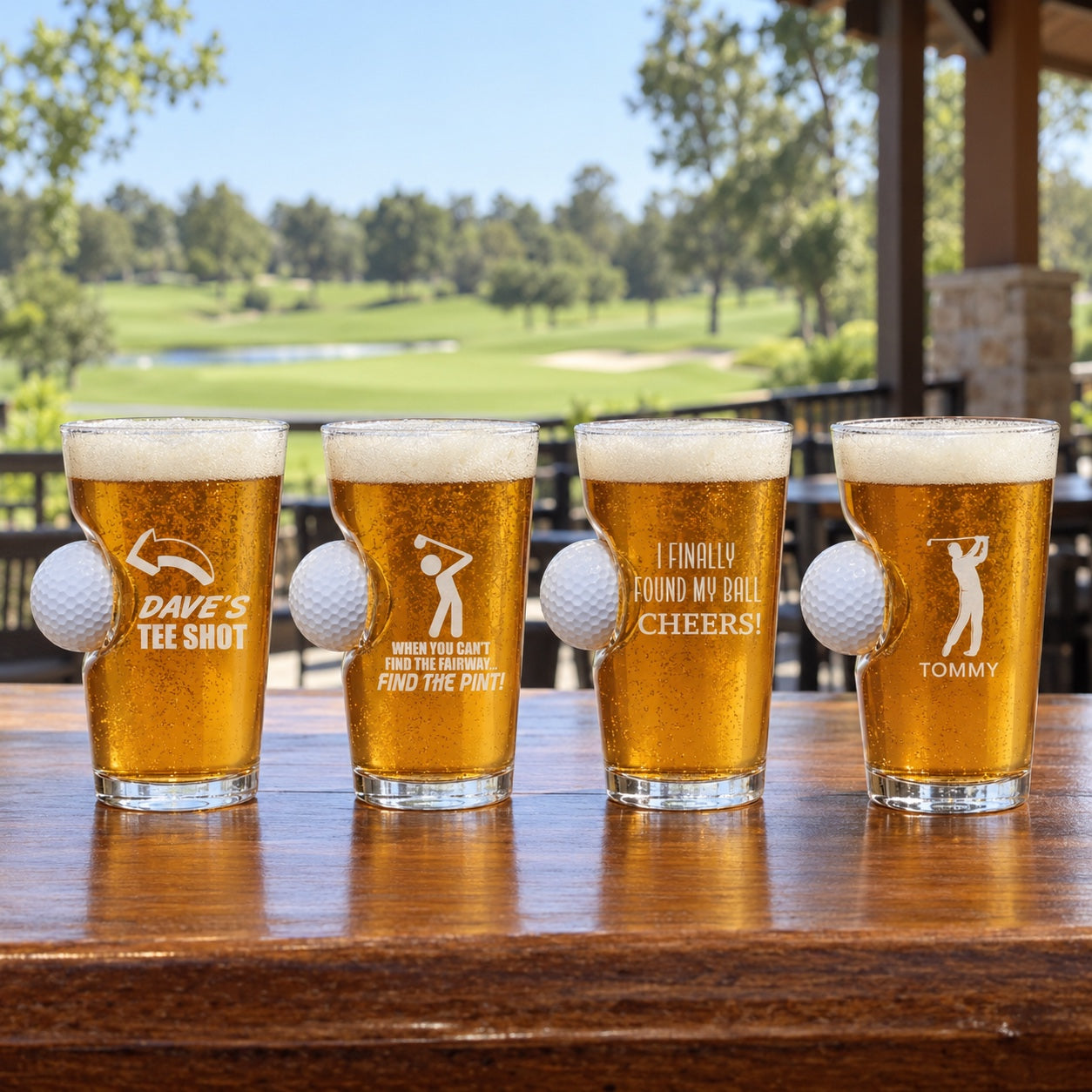 Golf pint glass full of amber ale with a real golf ball set into the side, printed with an arrow and MIKE'S TEE SHOT, on a clubhouse patio