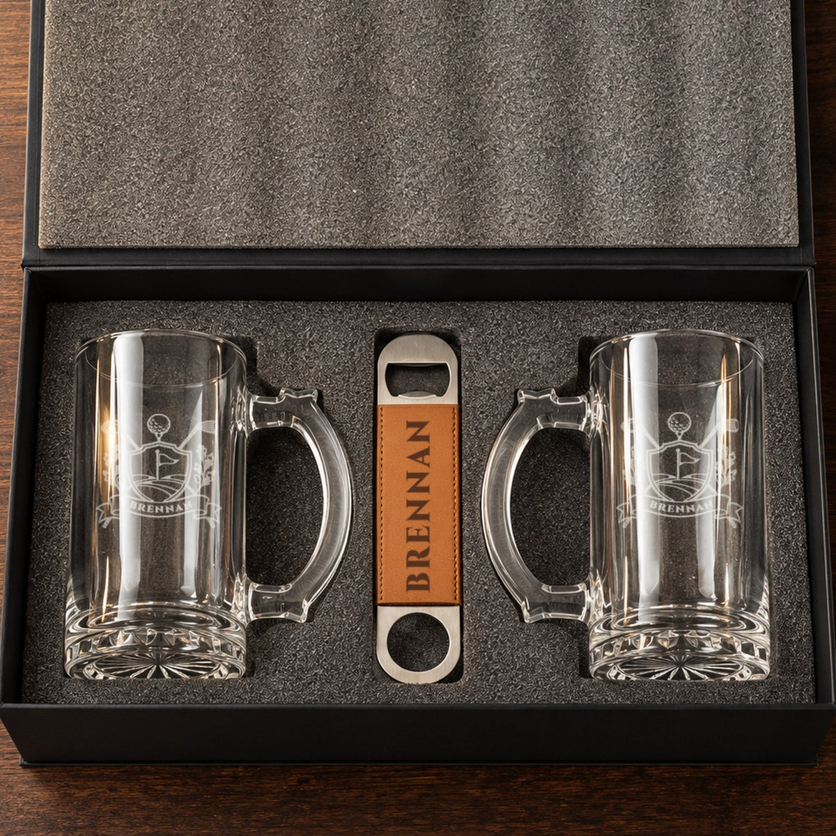 Golf beer mug gift set open in its foam-lined box: two glass beer mugs etched with a golf crest and BRENNAN, plus an engraved bottle opener